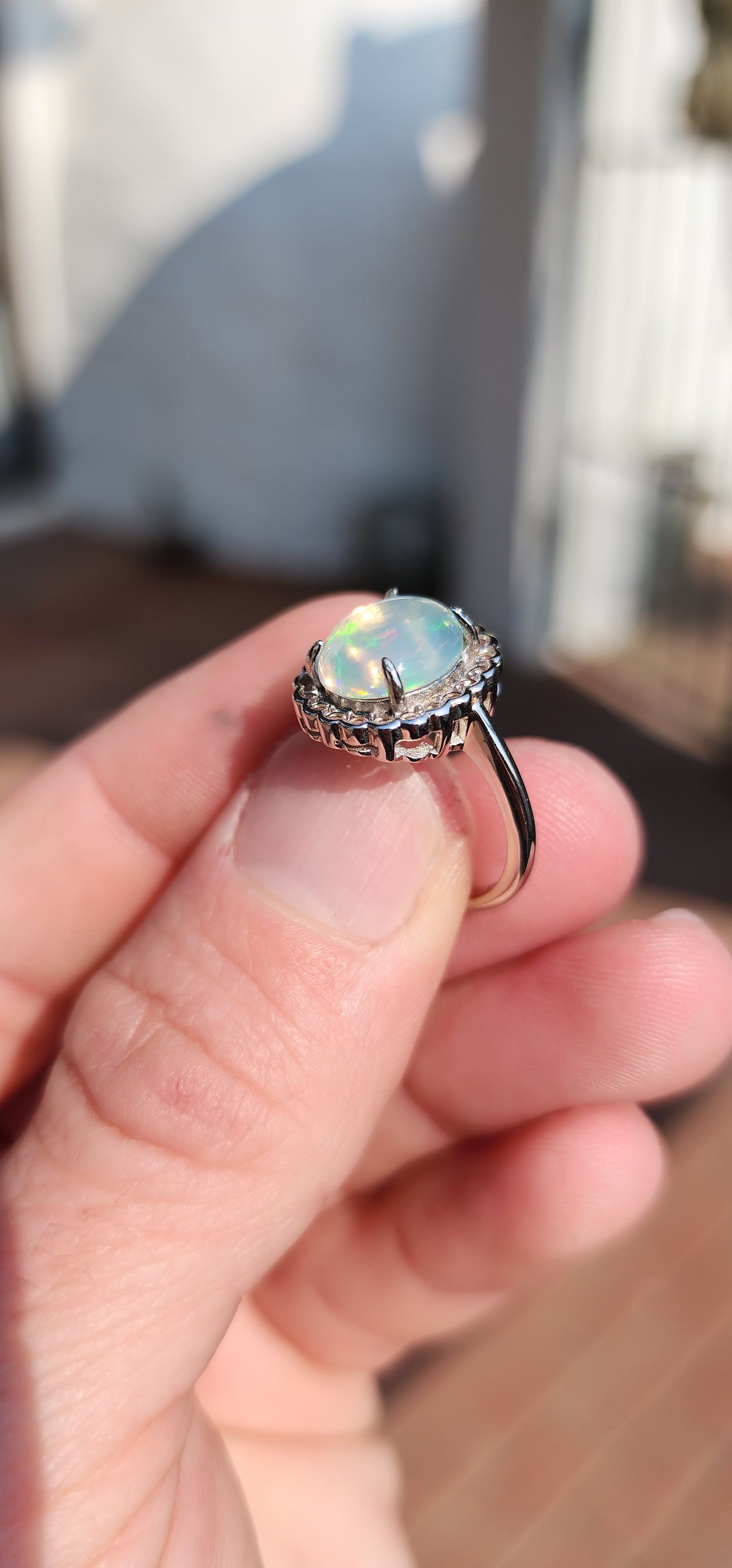 Impressive Ethiopian Water/Jelly Opal Cabochon and clear Round cut CZ haló Solitaire style ring .Crafted in Sterling Silver, the Oval Opal Cabochon is elegantly prong set and surrounded by an haló of 22x small Round cut CZ Gemstones.