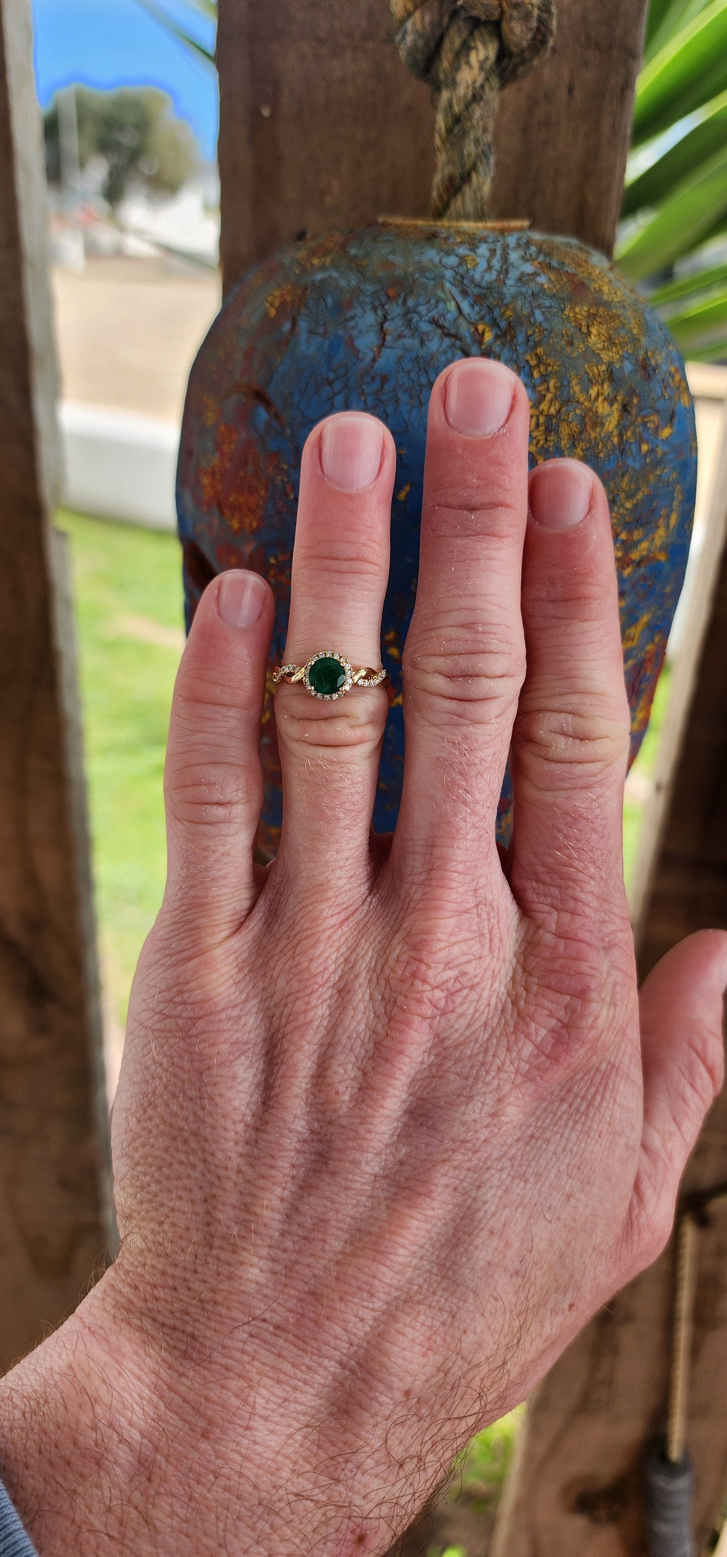 Exquisite 9ct Yellow Gold Crossover/Braided halo Ring, which boasts a mesmerizing prong set Round cut Emerald as its focal point,framed in a halo of small Brilliant Round cut Diamonds.