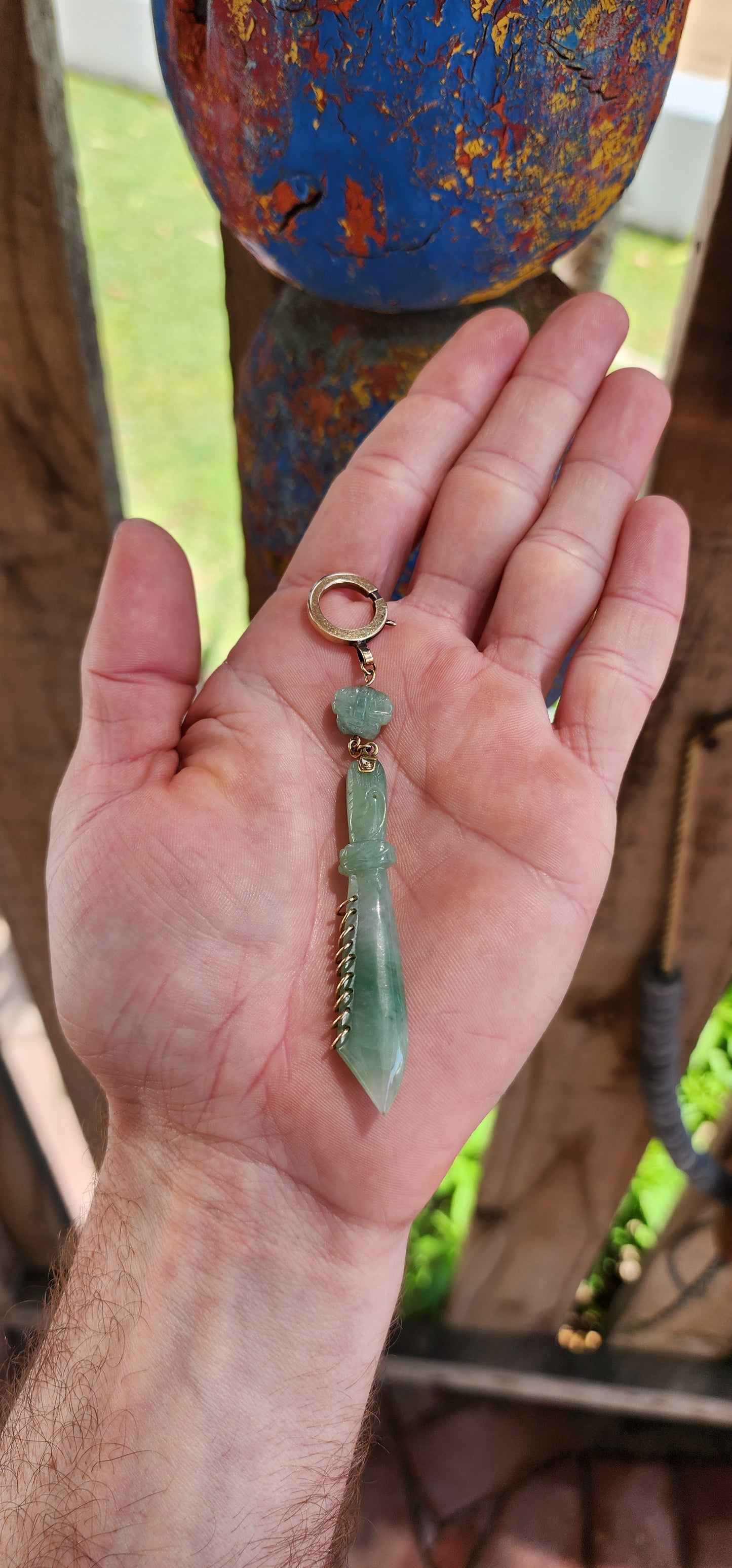 This pendant is a late Victorian-era piece featuring hand-carved jade and 9ct yellow gold. It’s crafted in the shape of a traditional Chinese nine-ring broadsword, with an apple-green jade blade.