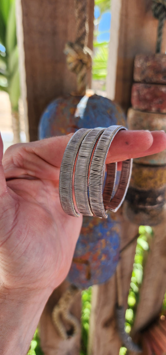 These bangles are a lot of three vintage Karen Hill Tribe open cuff bangles, crafted from solid 999 silver. Their weighty and solid nature, along with the intricate wrapped wire design, makes them unique pieces with both aesthetic and cultural value.