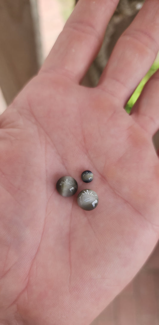 These three loose gemstones are cat's eye quartz cabochons, displaying the characteristic chatoyancy effect—a luminous band of light that moves across the surface when the stone is turned.