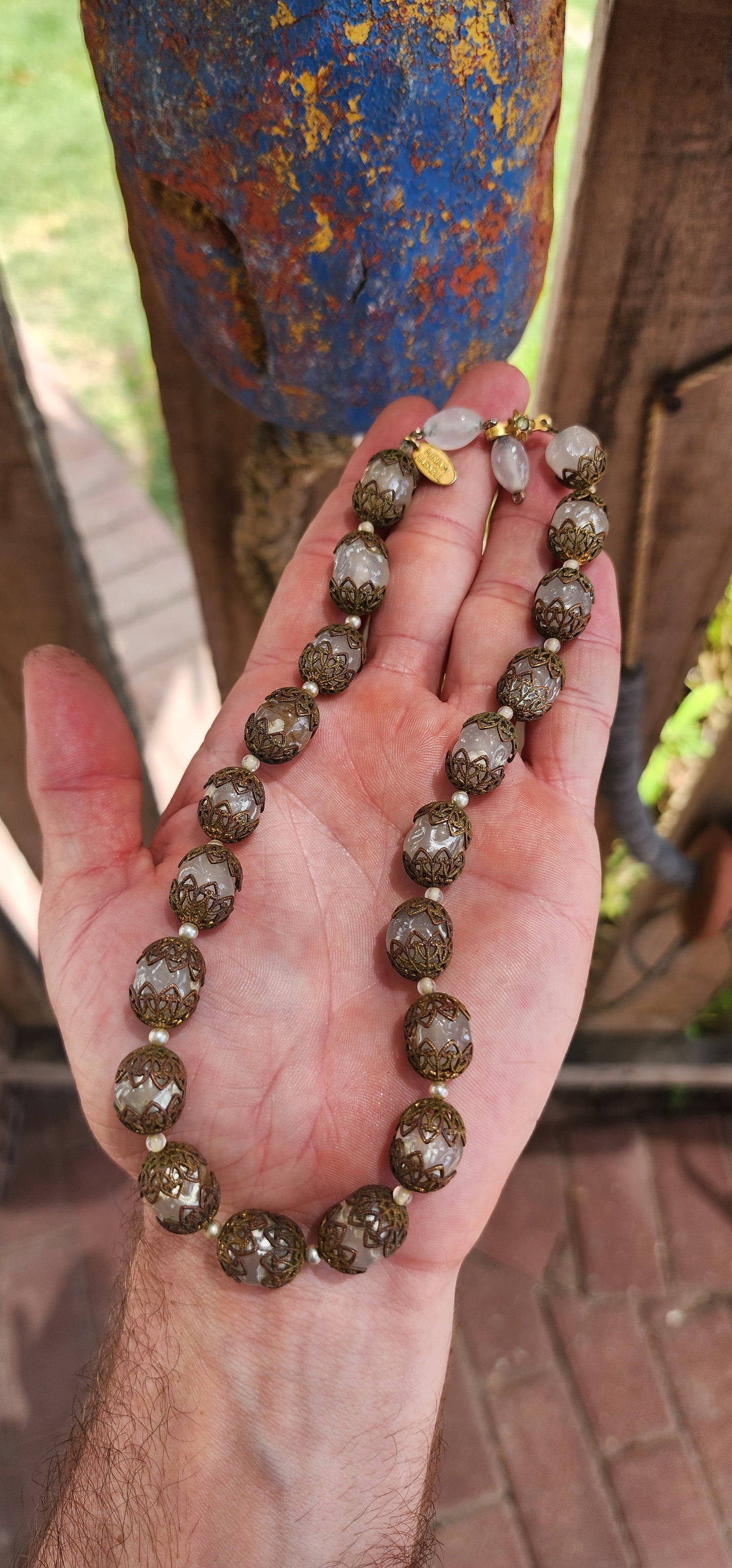 This exquisite Miriam Haskell costume necklace is a vintage choker-length piece from the 1970s, featuring opaque clear glass beads that are capped with ornate brass filigree.