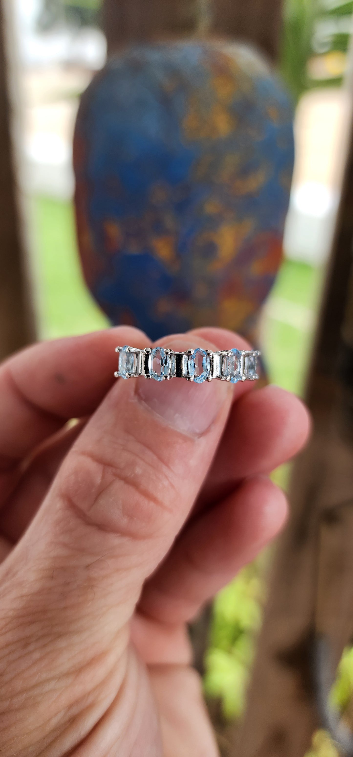 This sterling silver half-eternity ring is a refined and elegant piece, featuring five exquisite oval-cut sky blue topaz gemstones in a prong setting. The stones are arranged in a continuous row across the top of the band.