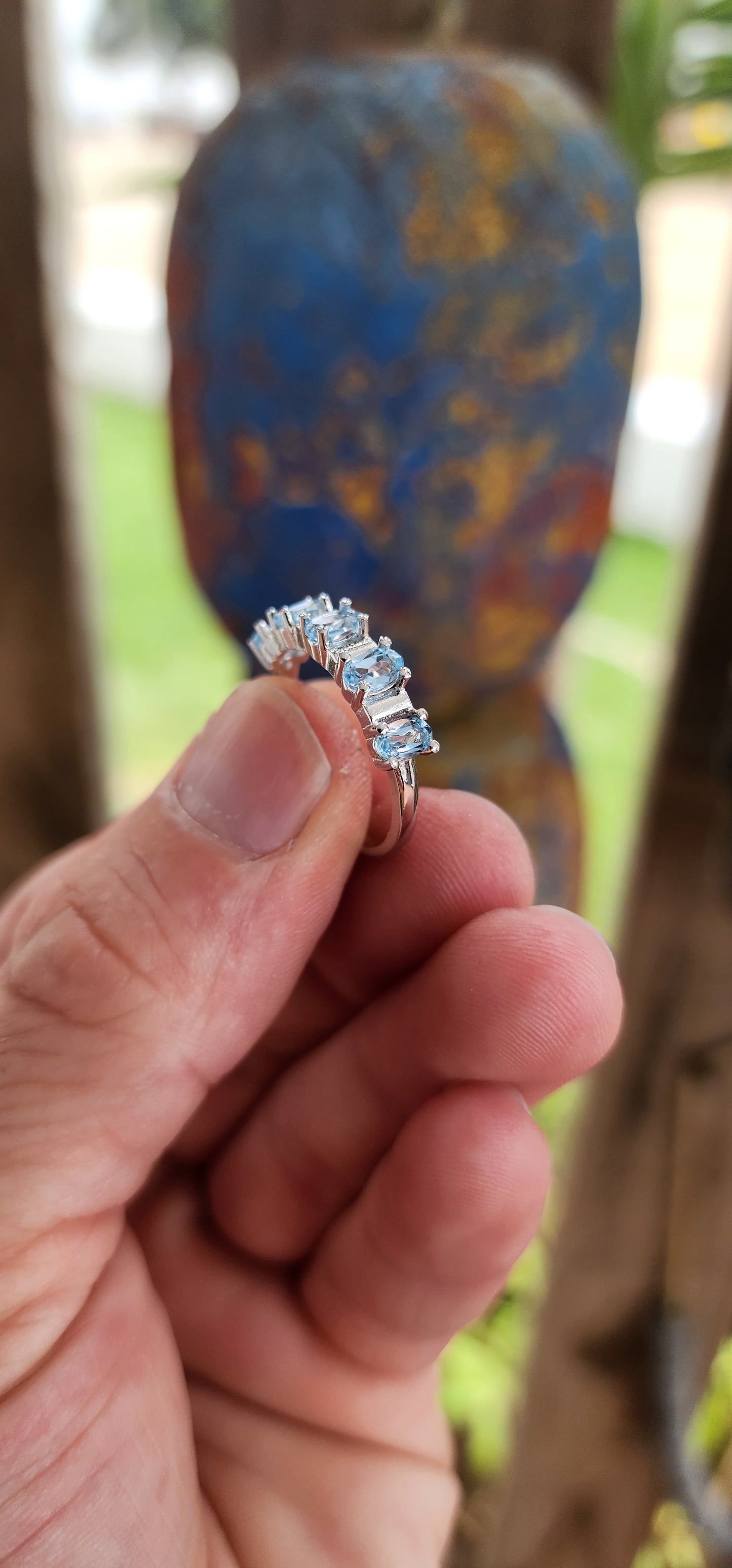 This sterling silver half-eternity ring is a refined and elegant piece, featuring five exquisite oval-cut sky blue topaz gemstones in a prong setting. The stones are arranged in a continuous row across the top of the band.