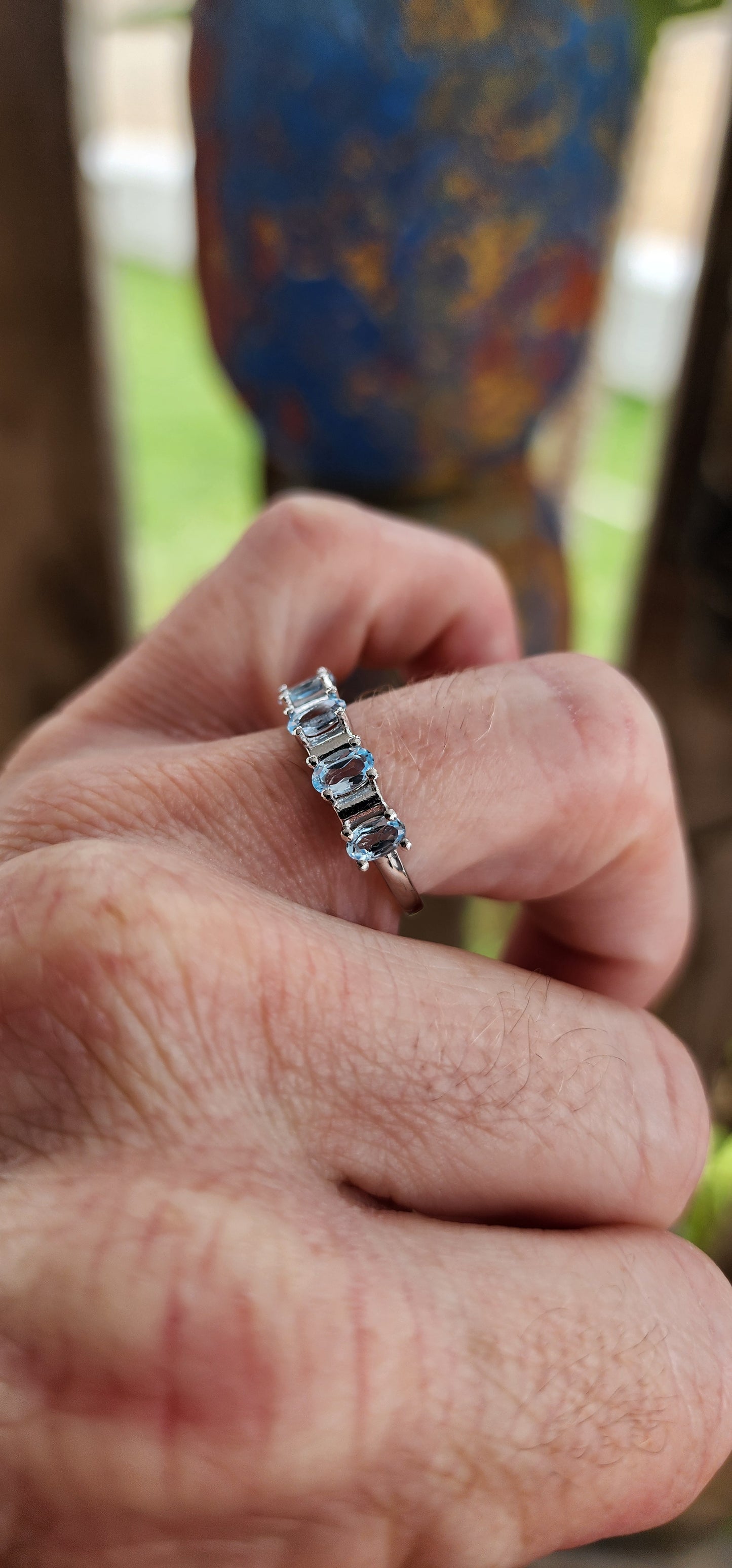 This sterling silver half-eternity ring is a refined and elegant piece, featuring five exquisite oval-cut sky blue topaz gemstones in a prong setting. The stones are arranged in a continuous row across the top of the band.