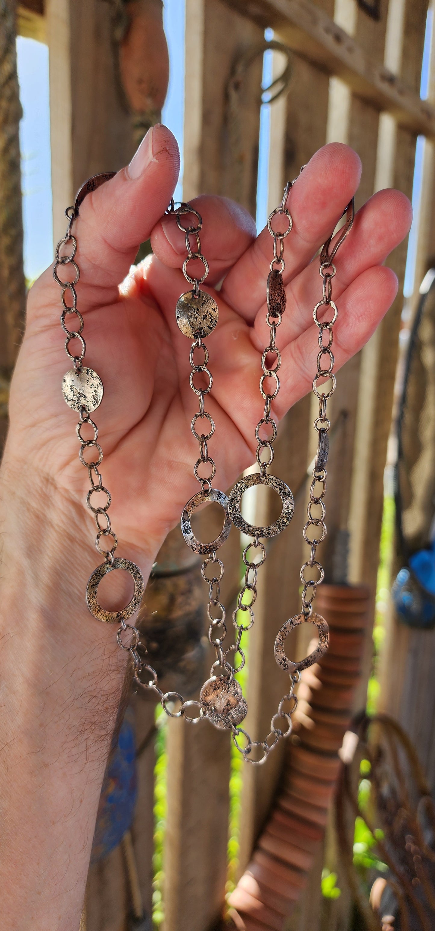 This necklace is a bold, free-spirited statement piece that dances between modernist minimalism and raw, textural brutality. Crafted from sterling silver, it showcases a mesmerizing interplay of hammered, textured, and patinated surfaces.