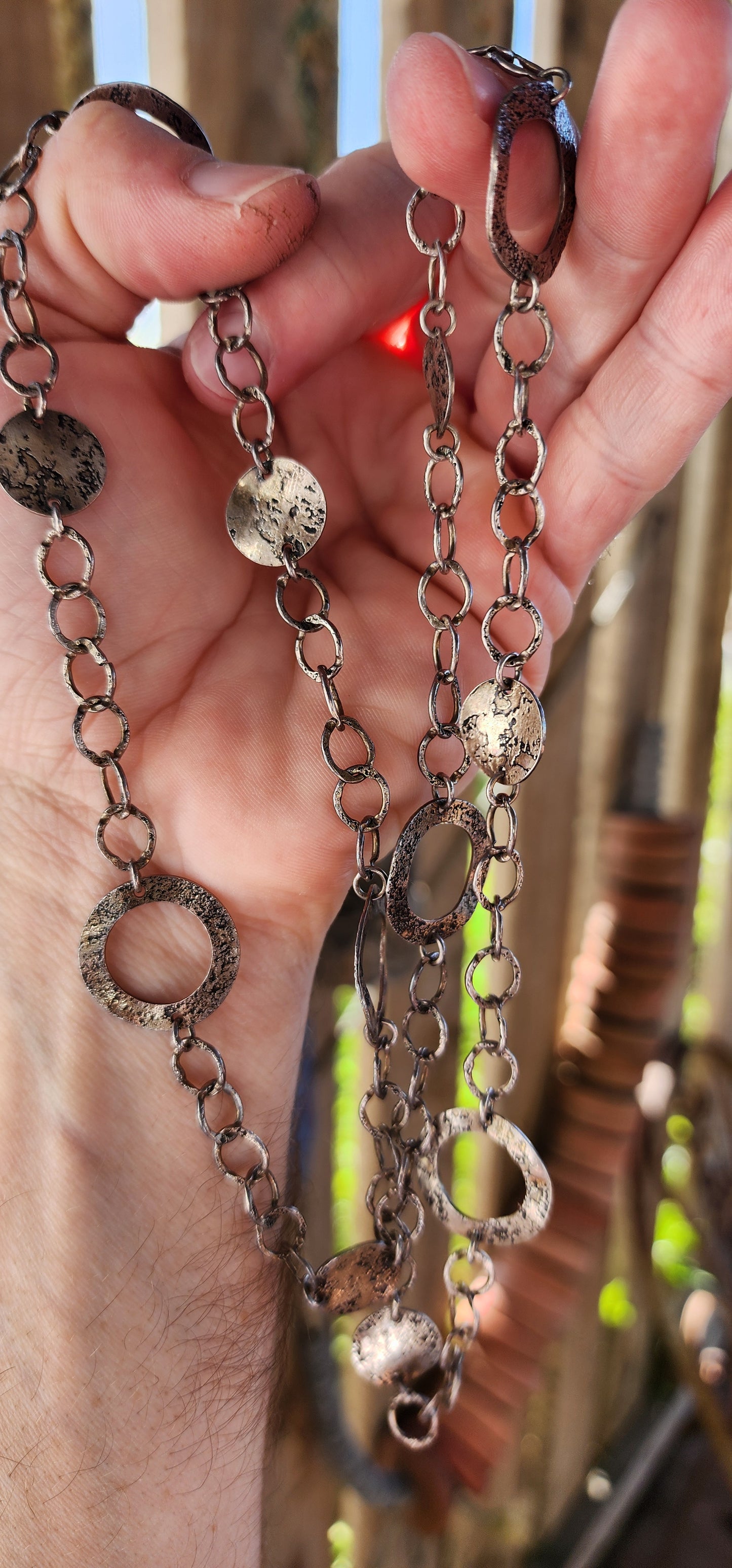 This necklace is a bold, free-spirited statement piece that dances between modernist minimalism and raw, textural brutality. Crafted from sterling silver, it showcases a mesmerizing interplay of hammered, textured, and patinated surfaces.