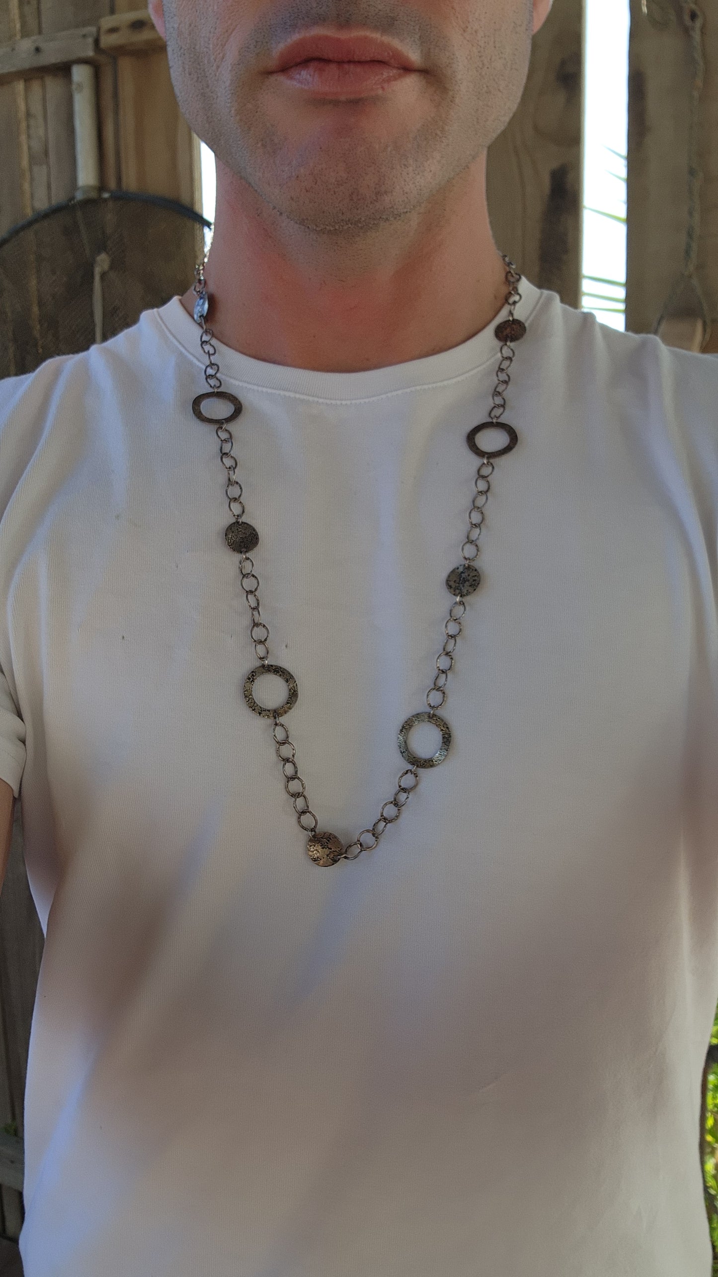 This necklace is a bold, free-spirited statement piece that dances between modernist minimalism and raw, textural brutality. Crafted from sterling silver, it showcases a mesmerizing interplay of hammered, textured, and patinated surfaces.