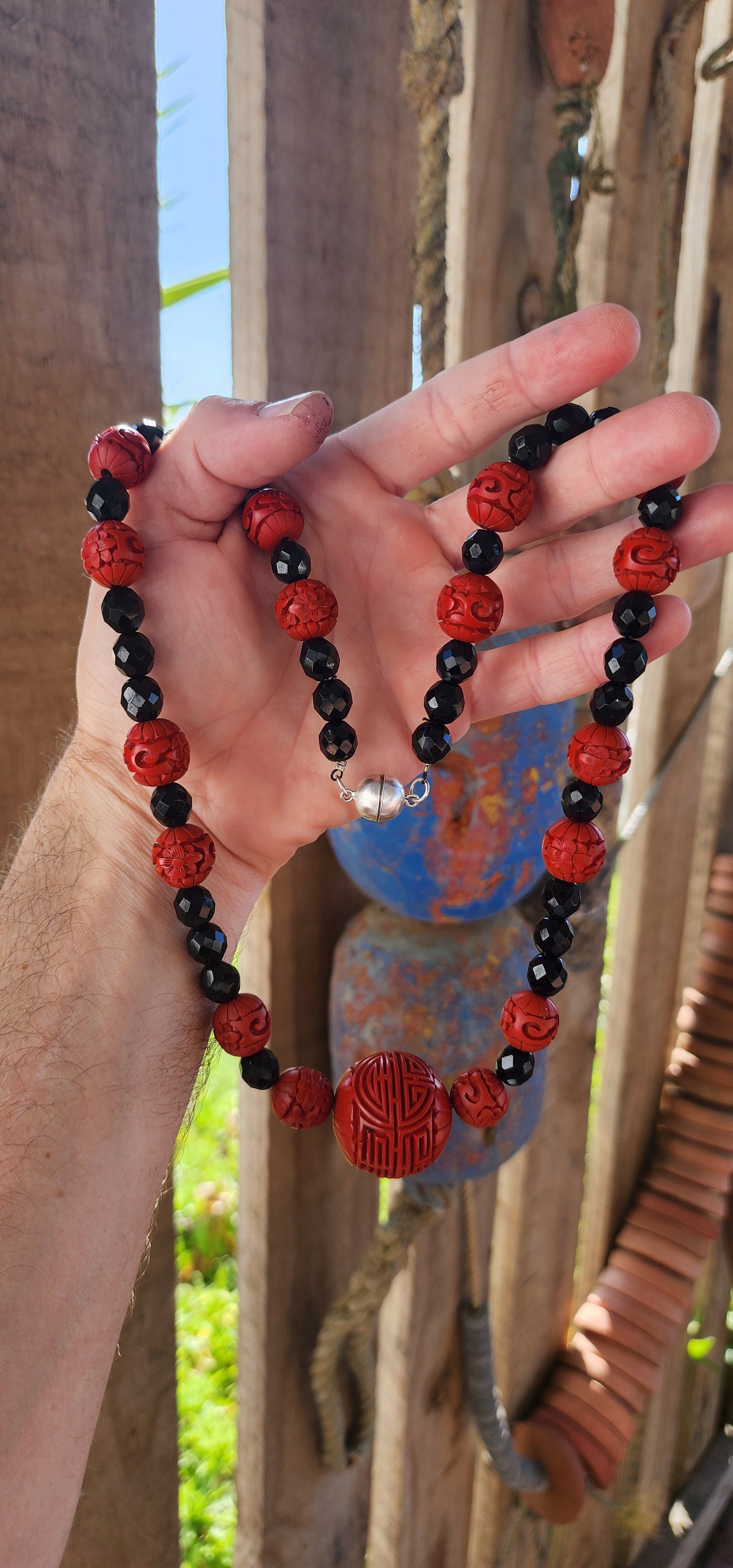 This vintage mid 20th century Chinese export necklace is a stunning example of traditional craftsmanship, featuring hand-carved cinnabar lacquer beads, faceted French jet glass beads, and a sterling silver magnetic clasp.