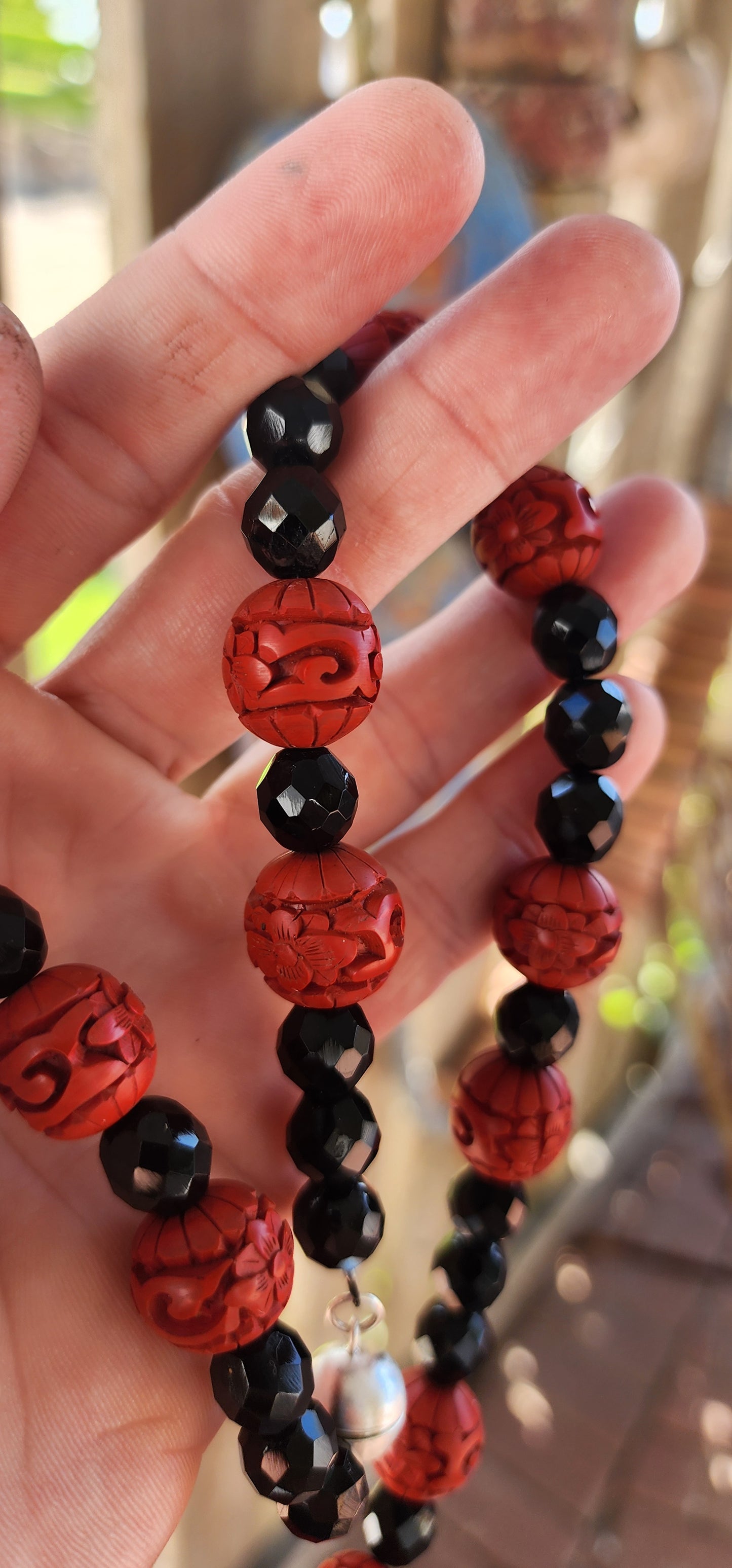 This vintage mid 20th century Chinese export necklace is a stunning example of traditional craftsmanship, featuring hand-carved cinnabar lacquer beads, faceted French jet glass beads, and a sterling silver magnetic clasp.