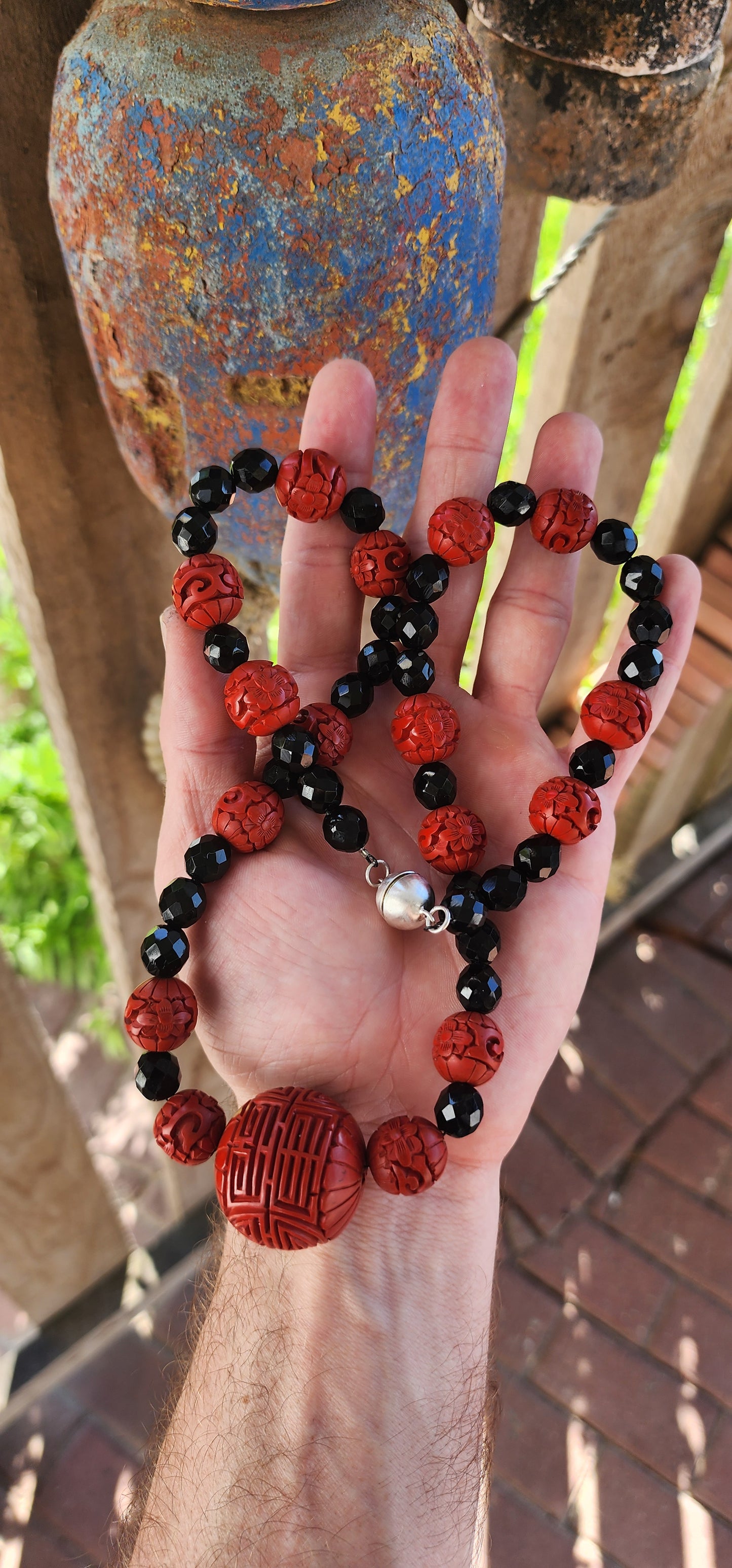 This vintage mid 20th century Chinese export necklace is a stunning example of traditional craftsmanship, featuring hand-carved cinnabar lacquer beads, faceted French jet glass beads, and a sterling silver magnetic clasp.