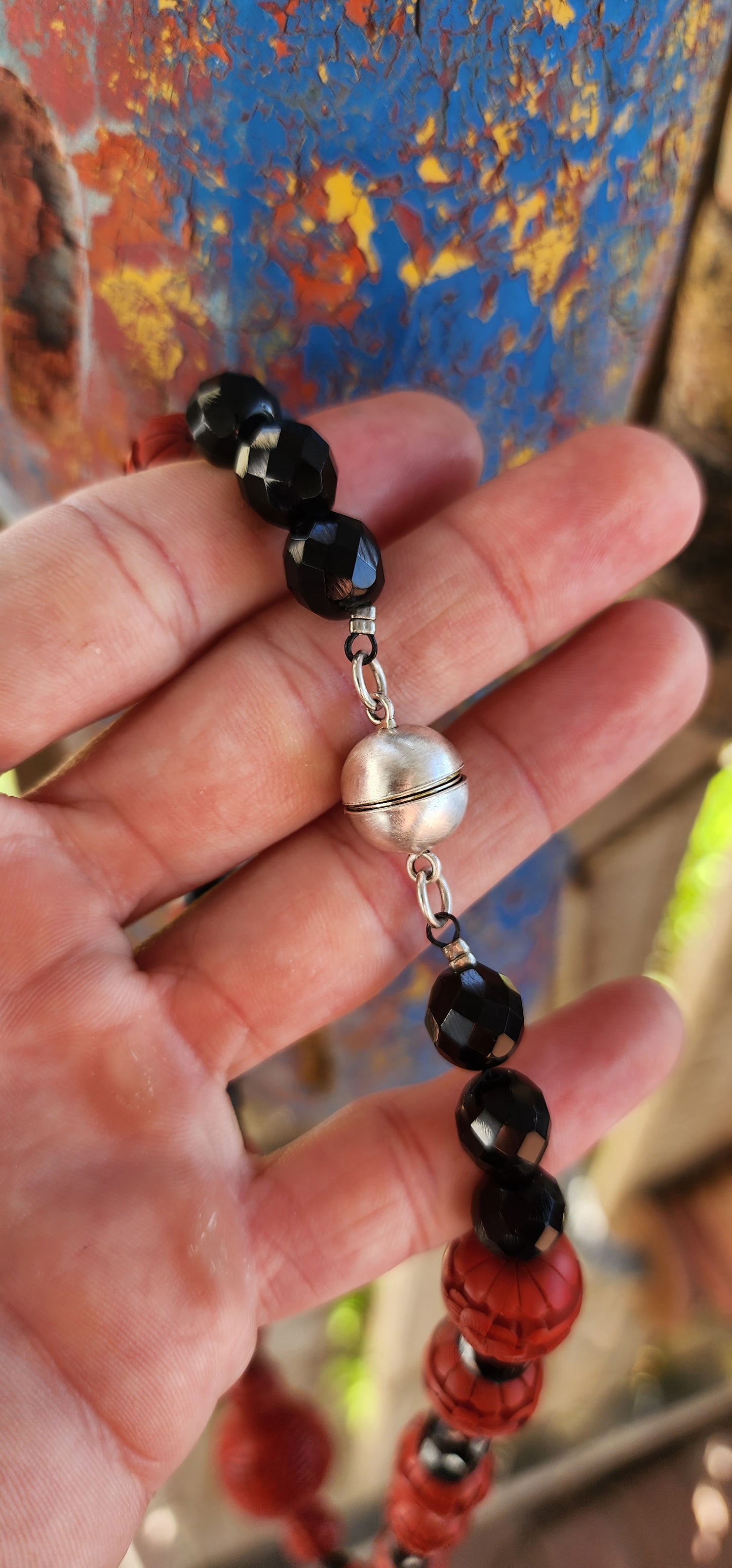 This vintage mid 20th century Chinese export necklace is a stunning example of traditional craftsmanship, featuring hand-carved cinnabar lacquer beads, faceted French jet glass beads, and a sterling silver magnetic clasp.