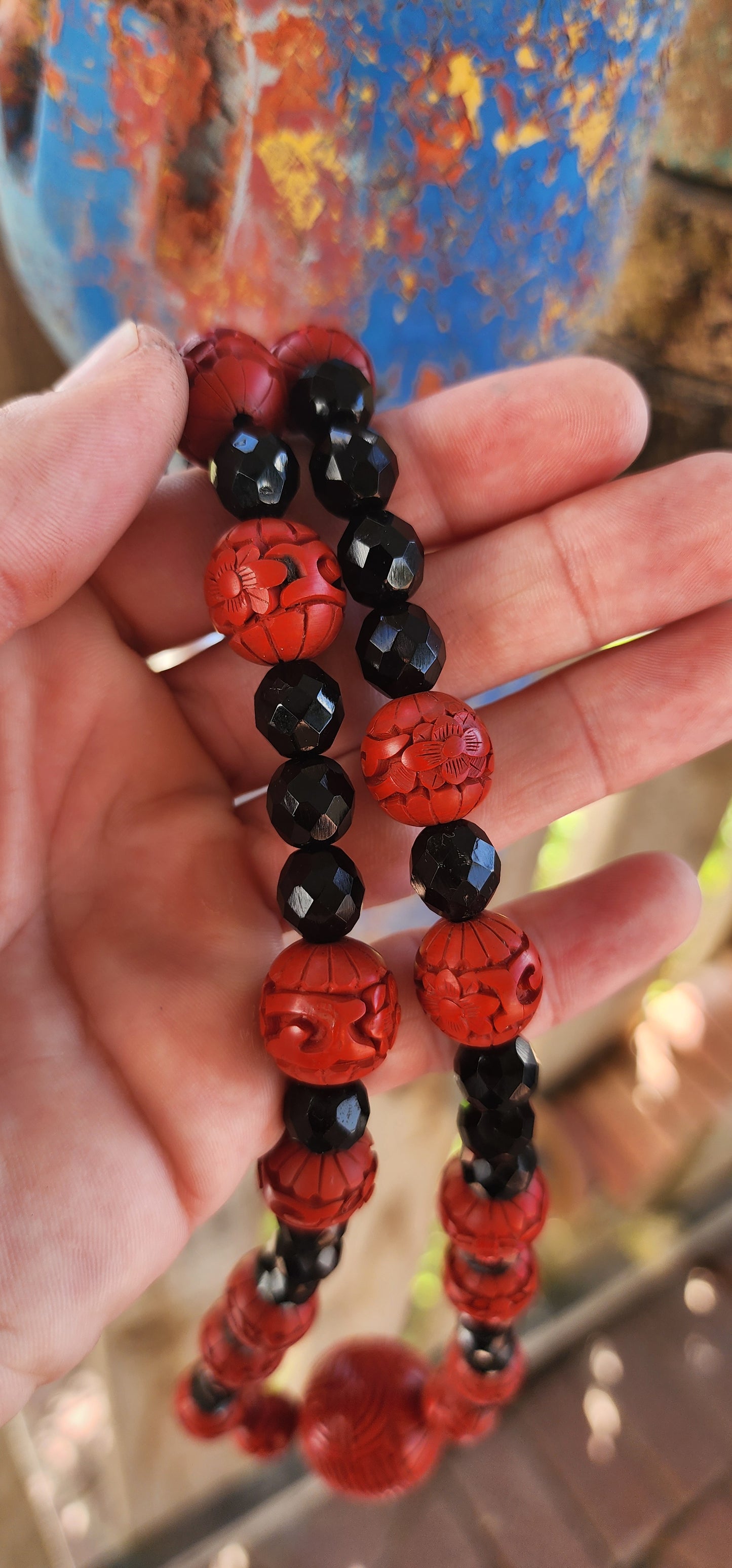 This vintage mid 20th century Chinese export necklace is a stunning example of traditional craftsmanship, featuring hand-carved cinnabar lacquer beads, faceted French jet glass beads, and a sterling silver magnetic clasp.