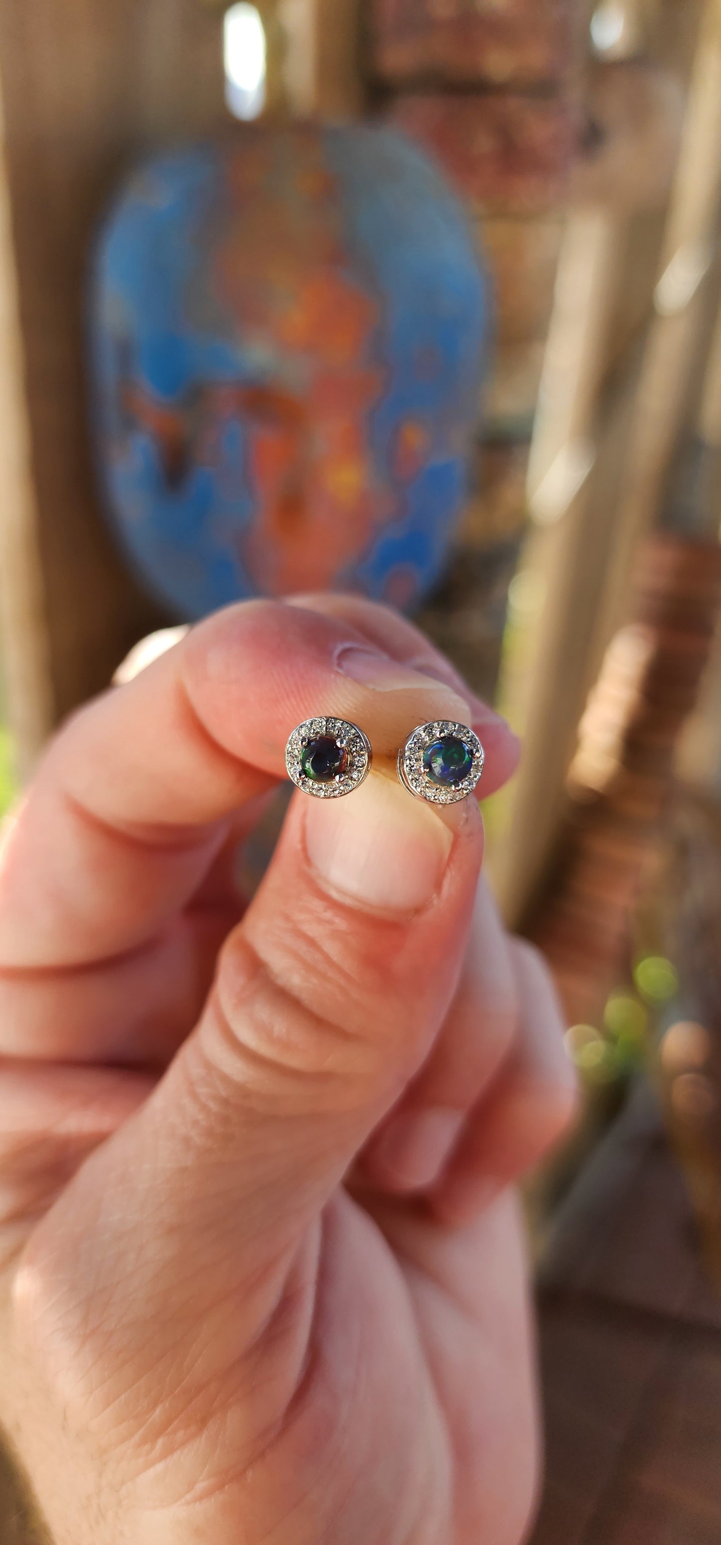 These exquisite Ethiopian black opal halo stud earrings exude classical elegance and refined beauty. Fashioned from sterling silver, each earring showcases a mesmerizing round-cut black opal cabochon, held securely in a delicate prong setting.