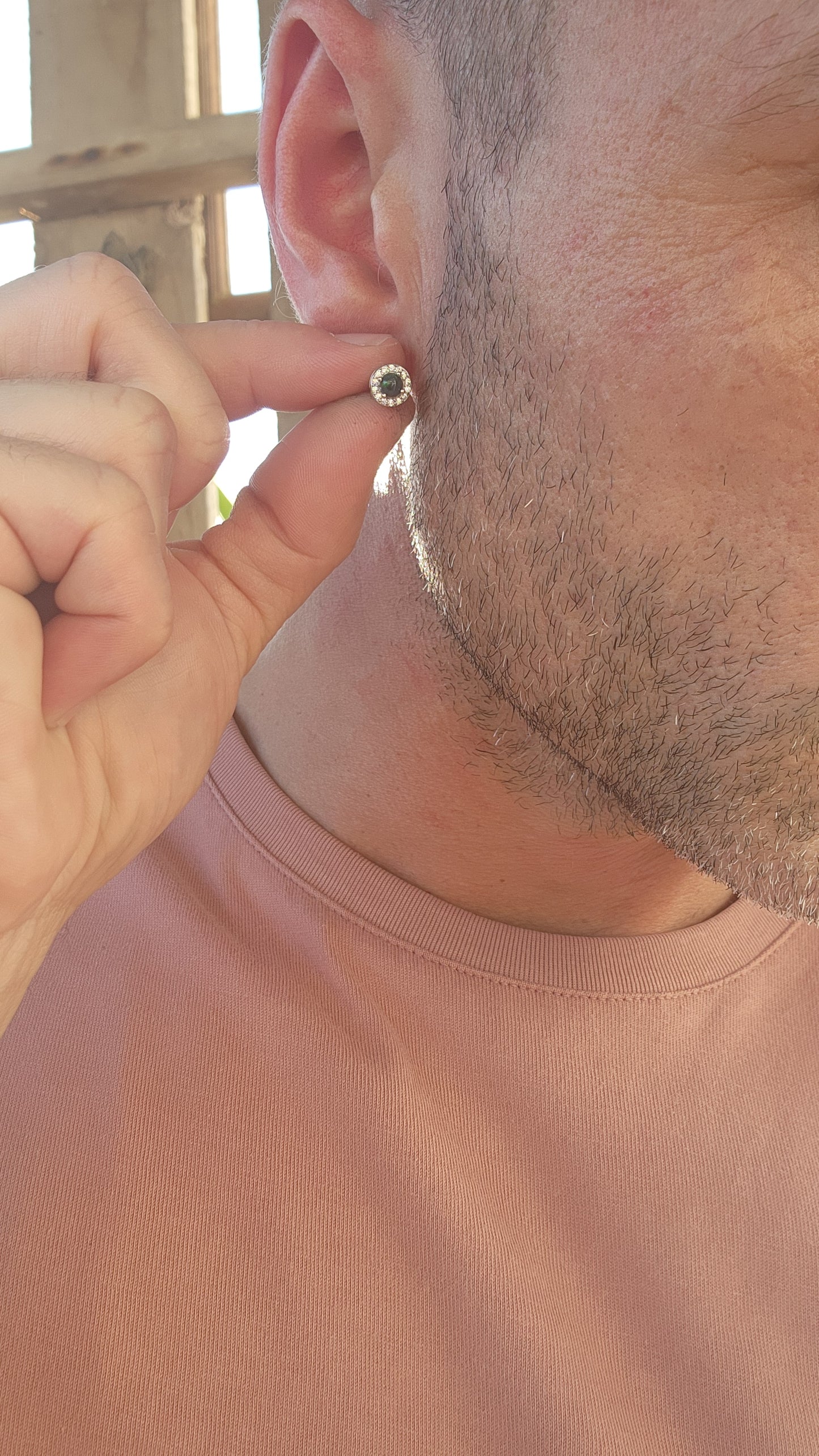 These exquisite Ethiopian black opal halo stud earrings exude classical elegance and refined beauty. Fashioned from sterling silver, each earring showcases a mesmerizing round-cut black opal cabochon, held securely in a delicate prong setting.
