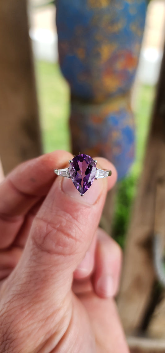 Prepare to be enchanted — this sterling silver trilogy ring is pure majesty wrapped in violet fire and classic elegance!