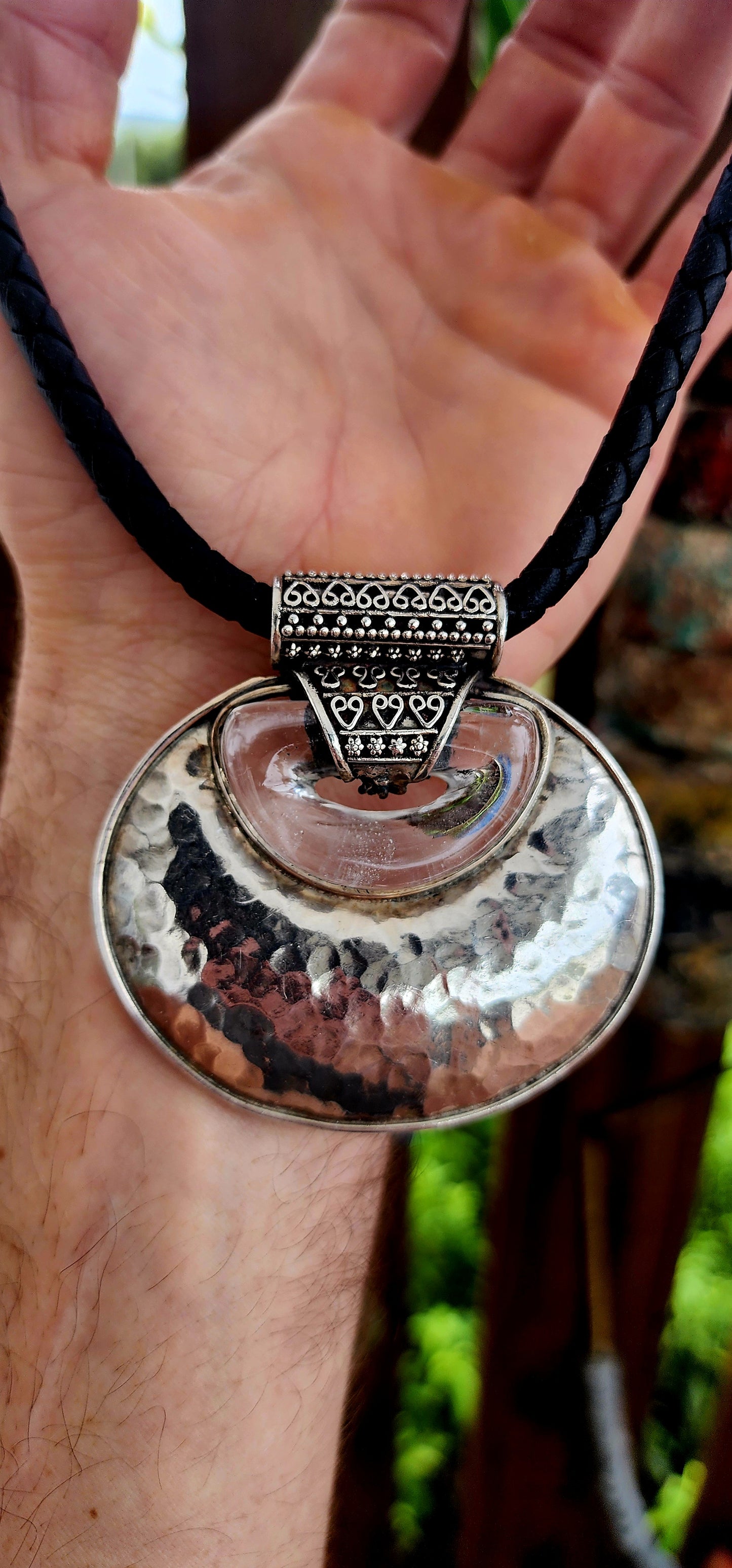 This is a bold, ethnic-inspired statement necklace that showcases a powerful artisanal aesthetic. The necklace centers on a dramatic pendant featuring a large, domed, oval-shaped disc crafted from hammered sterling silver.