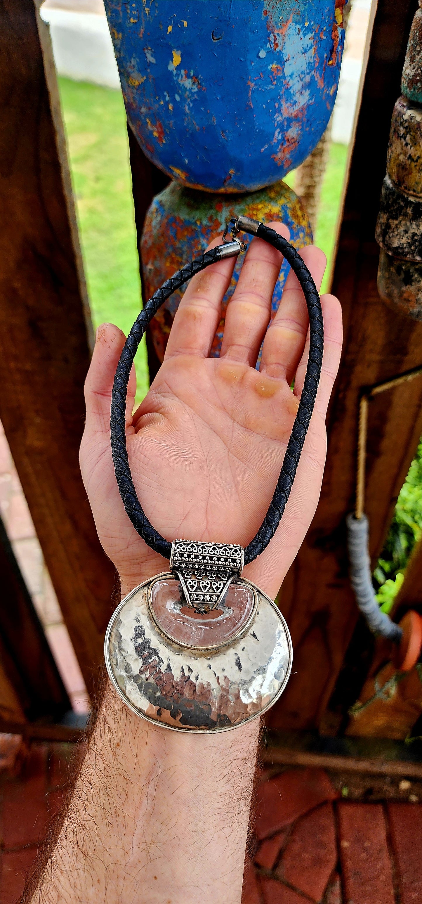 This is a bold, ethnic-inspired statement necklace that showcases a powerful artisanal aesthetic. The necklace centers on a dramatic pendant featuring a large, domed, oval-shaped disc crafted from hammered sterling silver.