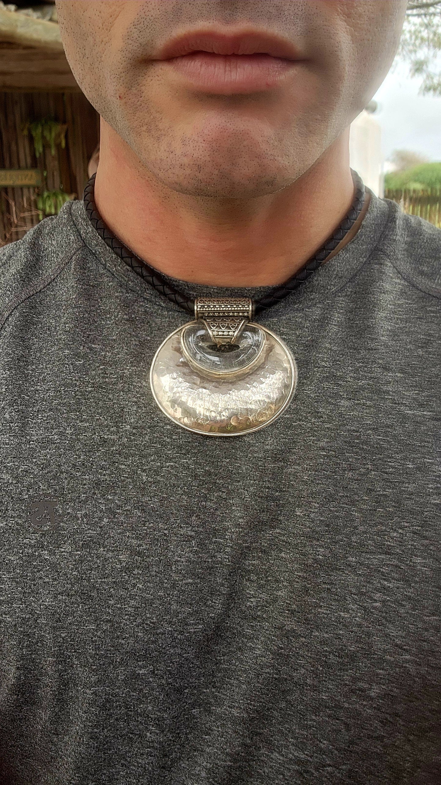 This is a bold, ethnic-inspired statement necklace that showcases a powerful artisanal aesthetic. The necklace centers on a dramatic pendant featuring a large, domed, oval-shaped disc crafted from hammered sterling silver.