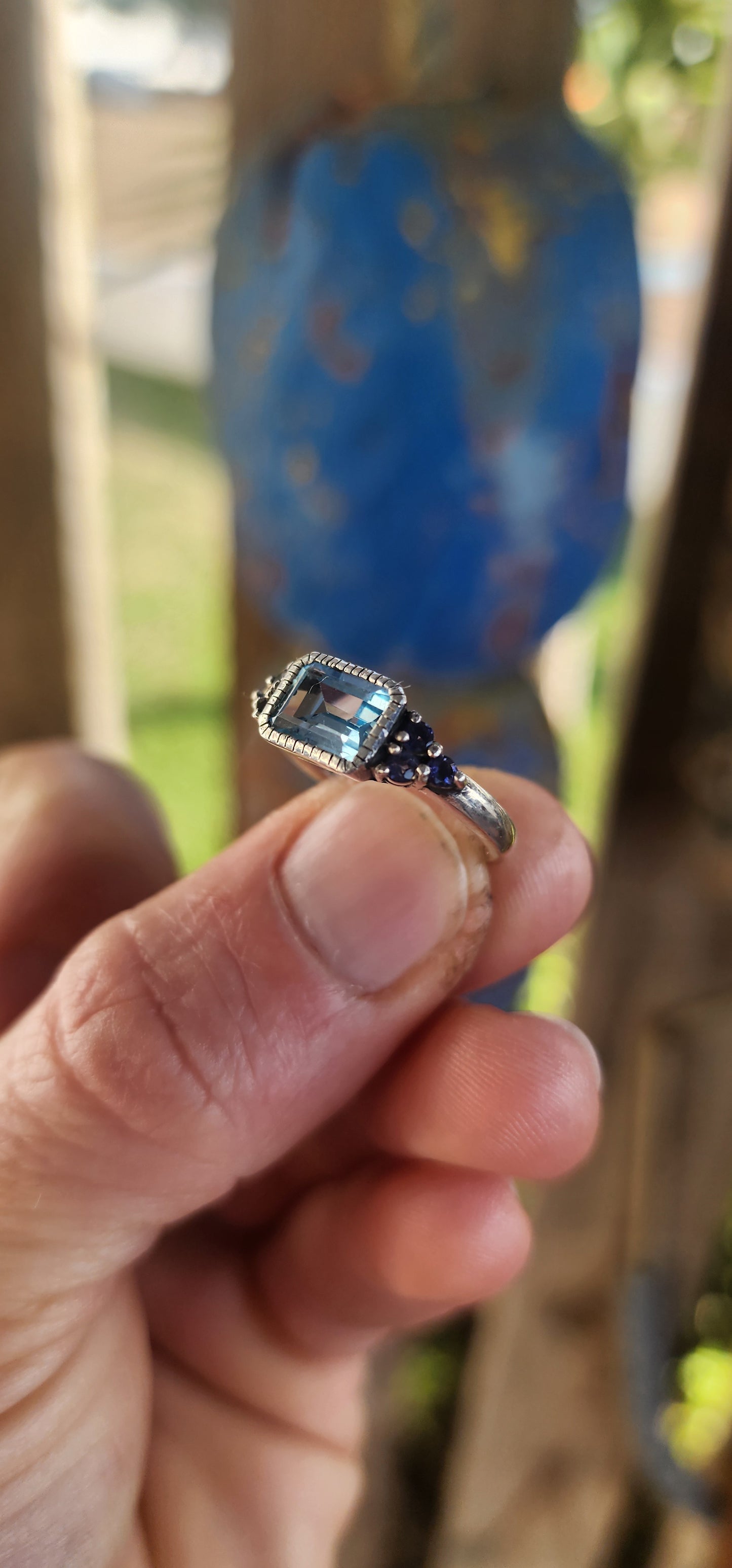 A delicate balance of clarity, color, and craftsmanship, this elegant trilogy-style stacking ring is crafted in sterling silver. At its heart lies a captivating emerald-cut sky blue topaz, its crystalline hue as refreshing as a cloudless morning sky.