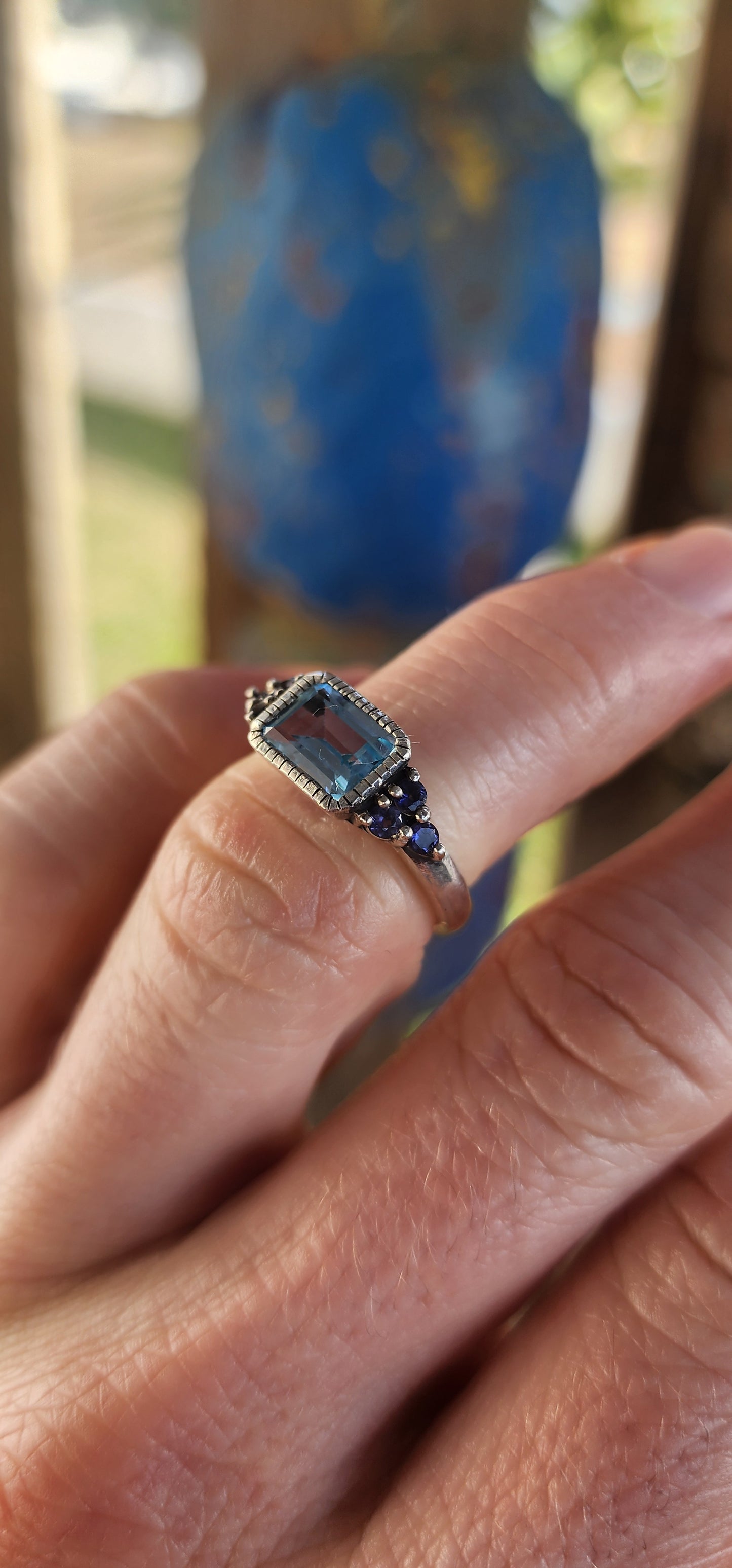 A delicate balance of clarity, color, and craftsmanship, this elegant trilogy-style stacking ring is crafted in sterling silver. At its heart lies a captivating emerald-cut sky blue topaz, its crystalline hue as refreshing as a cloudless morning sky.
