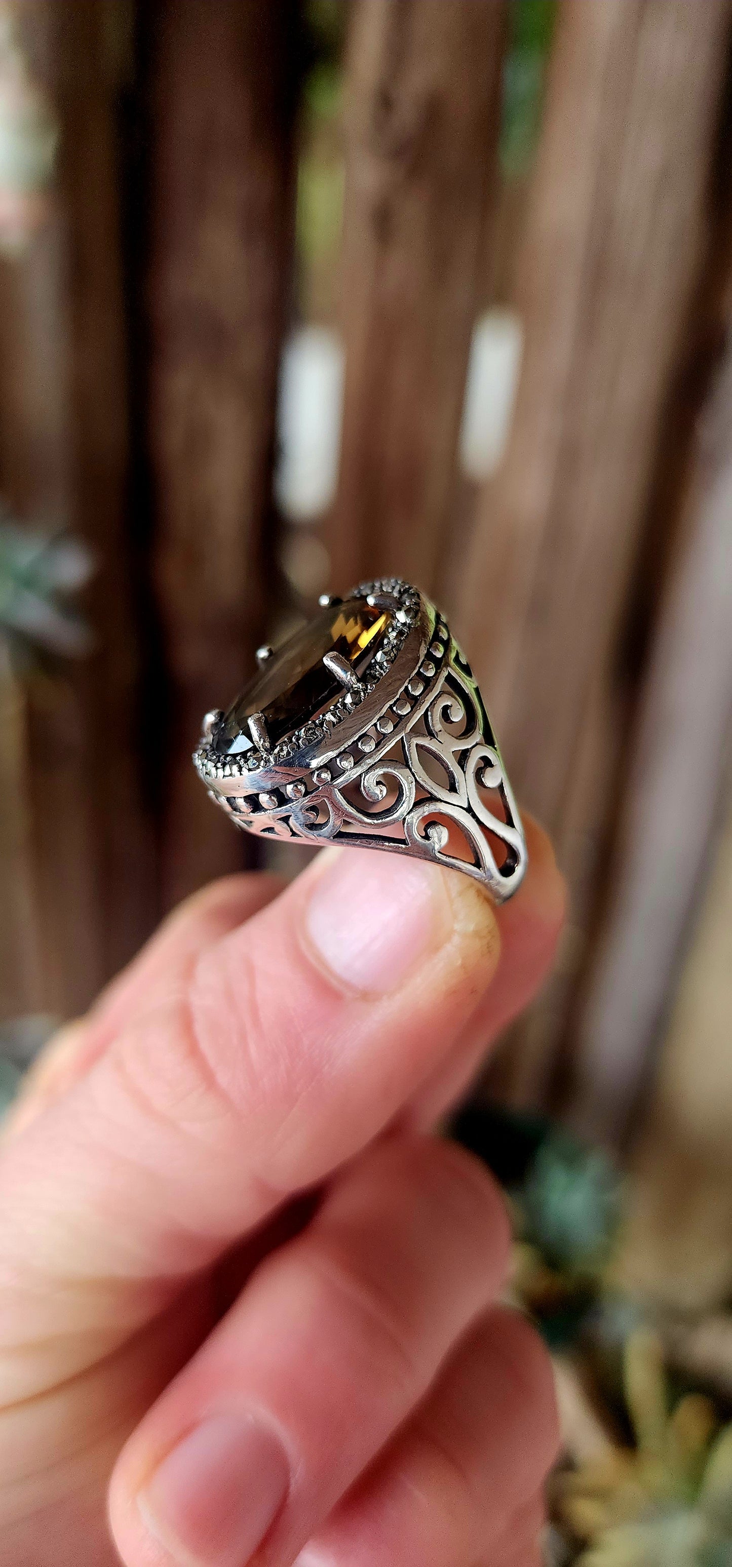 This bold and beautifully crafted sterling silver cocktail ring channels the grandeur of antique jewelry design. At its heart lies a large and rare oval-cut champagne/brown topaz.