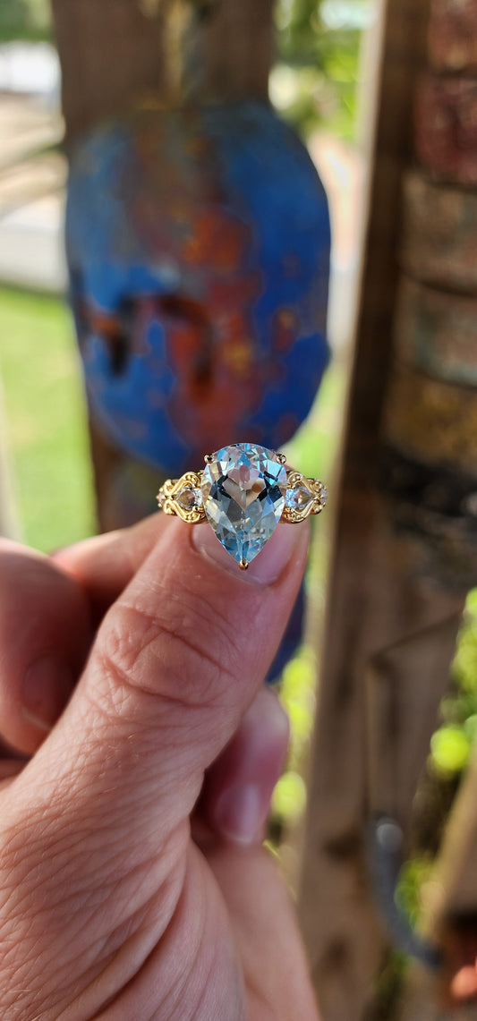 Ocean’s Crown – A Sky Blue Topaz Masterpiece.
Kissed by the ocean’s breath and wrapped in golden sunlight—this ring looks as though it was plucked from the treasure chest of a sea-born queen.