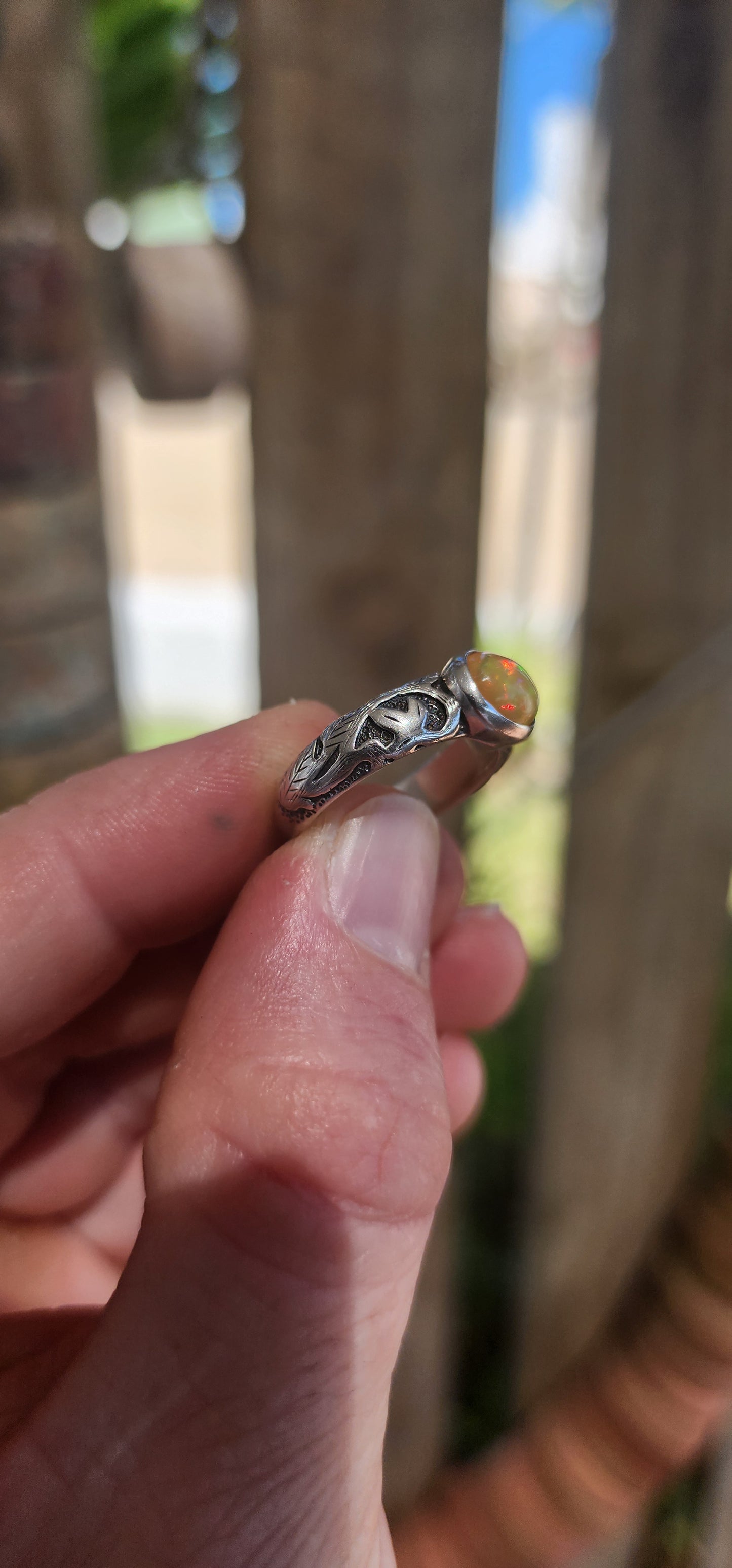 An absolutely mesmerizing handcrafted sterling silver ring featuring a luminous oval-cut Ethiopian fire opal cabochon, radiating with flickers of neon green, orange, and gold as it catches the light.