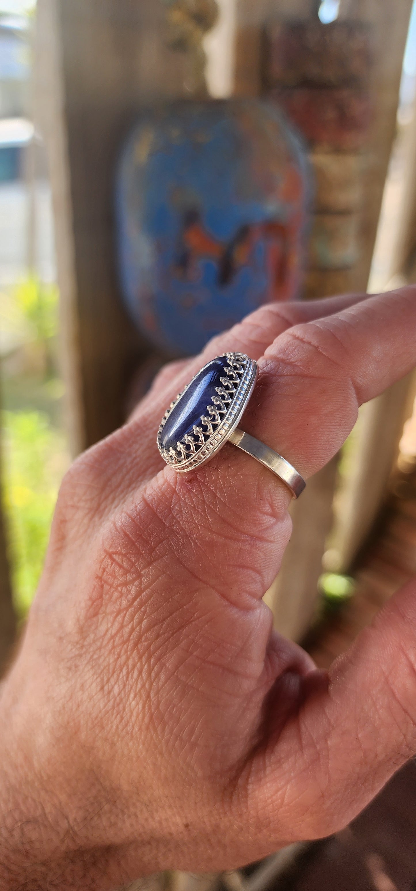 This artisan made sterling silver ring features a tumbled, organic-shaped blue sodalite gemstone, bezel-like cradled in ornate decorative claw prongs that look like a little crown around the stone.