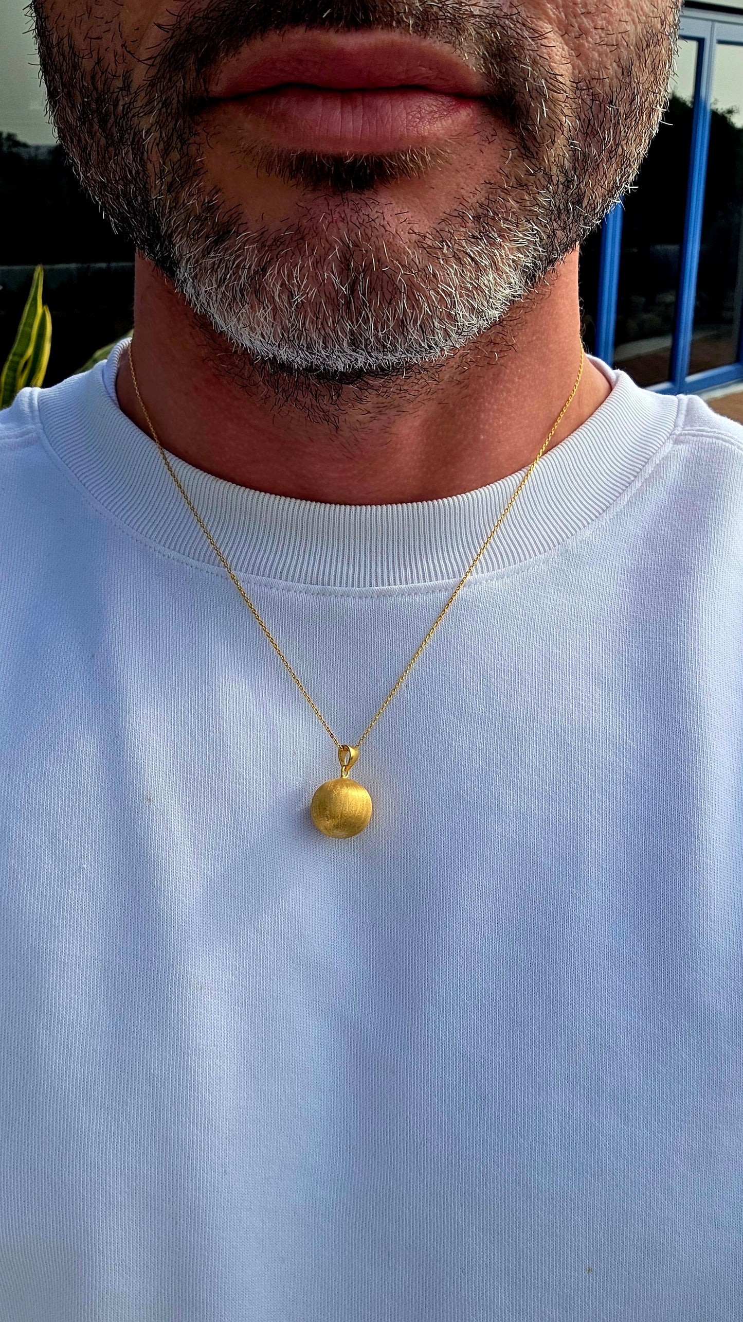 Crafted in sterling silver and finished with a luxurious layer of 18ct yellow gold plating, this striking pendant features a beautifully textured spherical orb with a soft satin finish that catches the light with a warm golden glow.