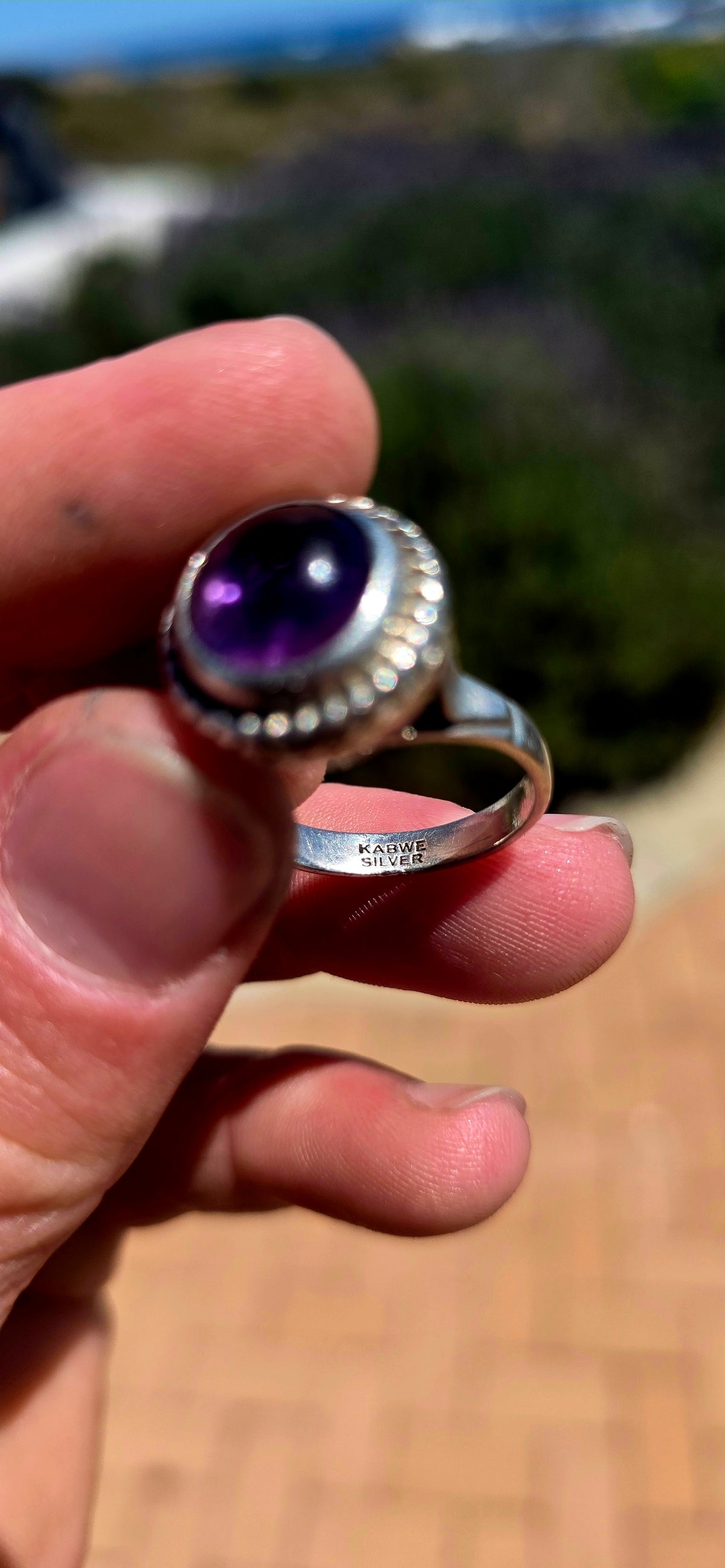 A striking handcrafted Kabwe sterling silver statement ring featuring a gorgeous, rounded purple amethyst cabochon, beautifully elevated within an elaborate sculptural silver setting.