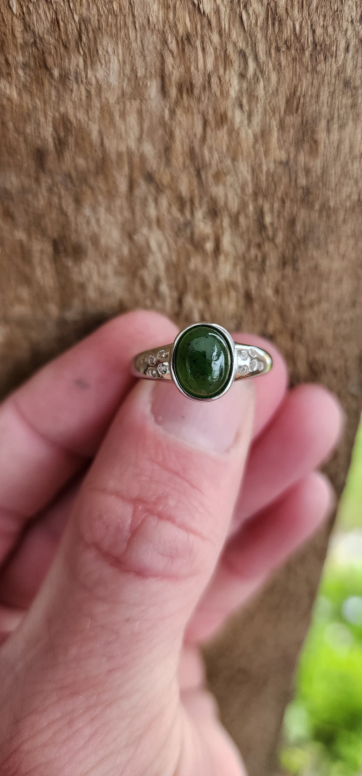 Sterling Silver Trilogy style ring bezel/tube set with a Oval shaped Green Nephrite Jade Cabochon in the centre and furthermore flush set with 5 x small CZ Gemstones on either side of the Jade Cabochon.