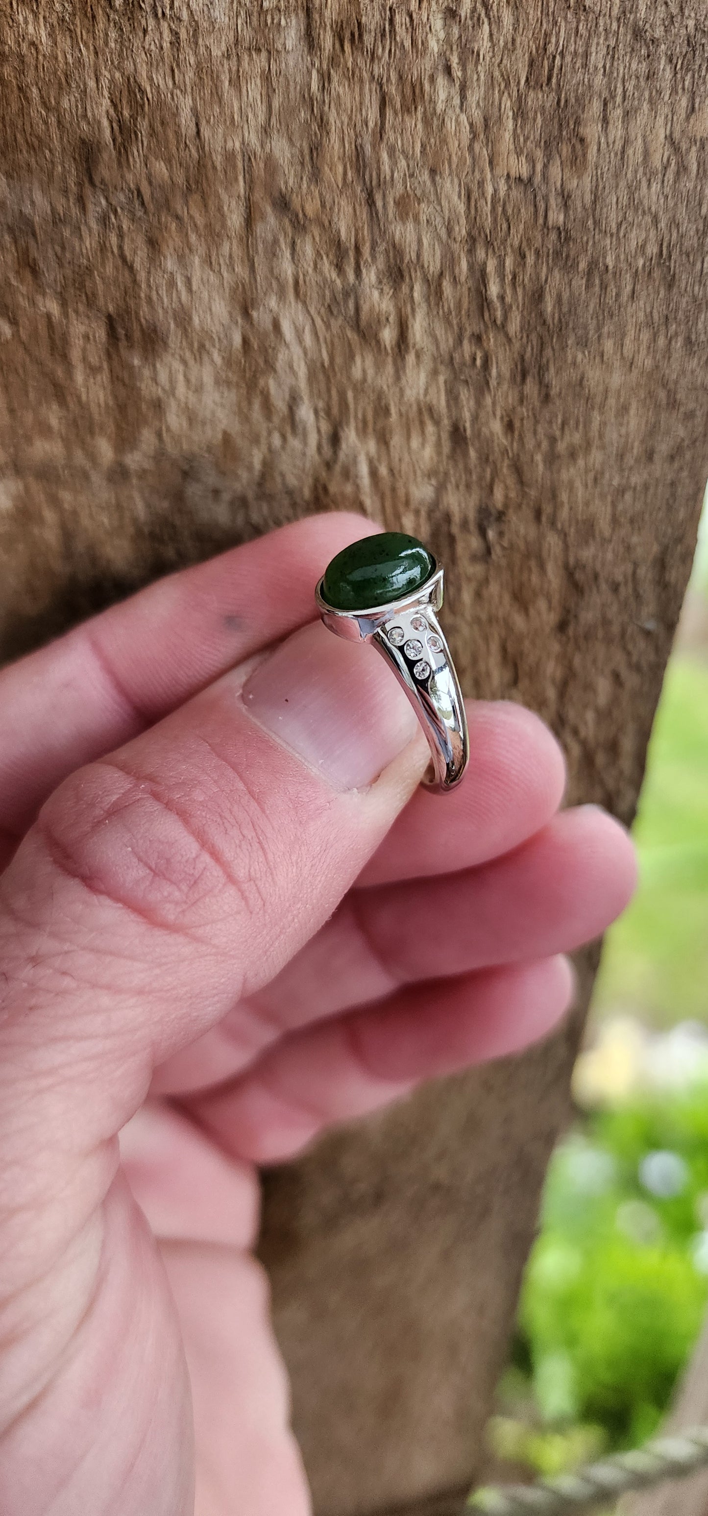 Sterling Silver Trilogy style ring bezel/tube set with a Oval shaped Green Nephrite Jade Cabochon in the centre and furthermore flush set with 5 x small CZ Gemstones on either side of the Jade Cabochon.