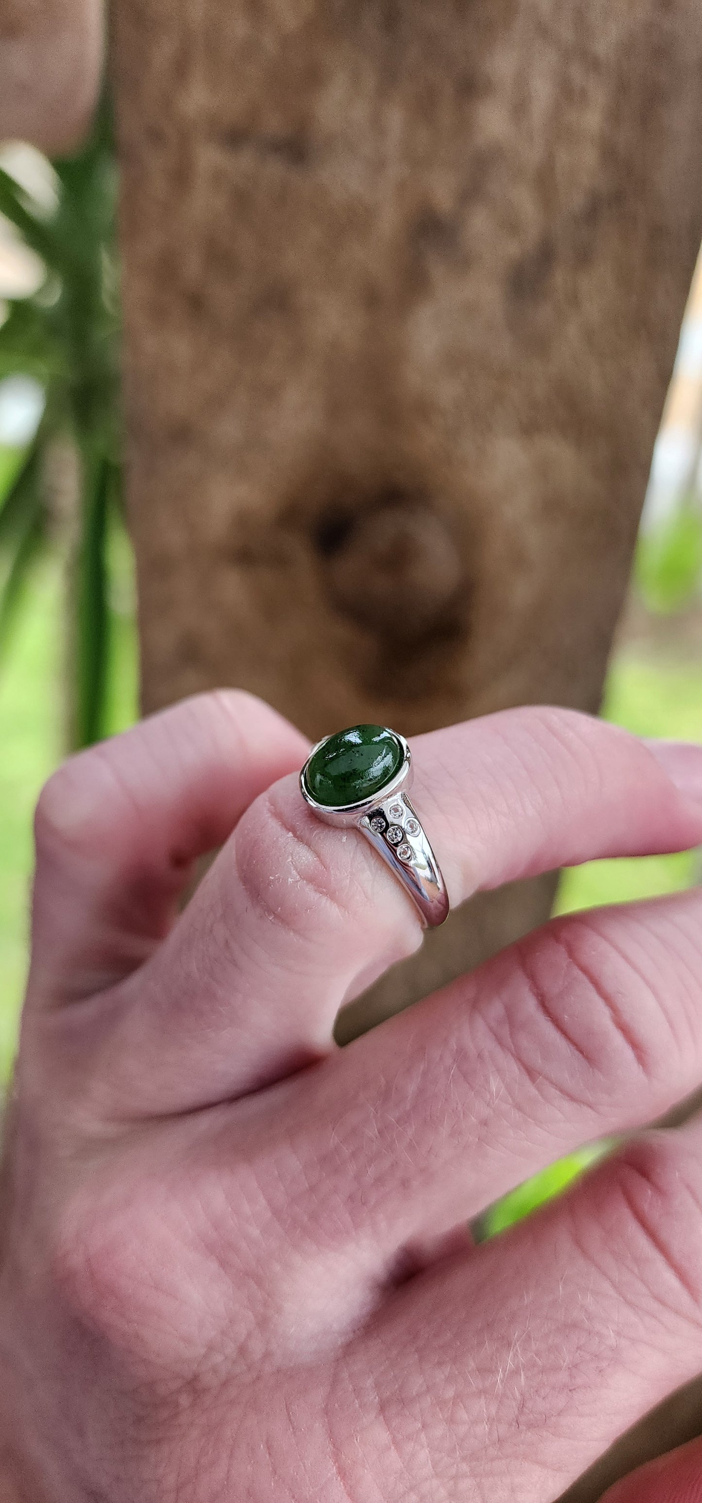 Sterling Silver Trilogy style ring bezel/tube set with a Oval shaped Green Nephrite Jade Cabochon in the centre and furthermore flush set with 5 x small CZ Gemstones on either side of the Jade Cabochon.