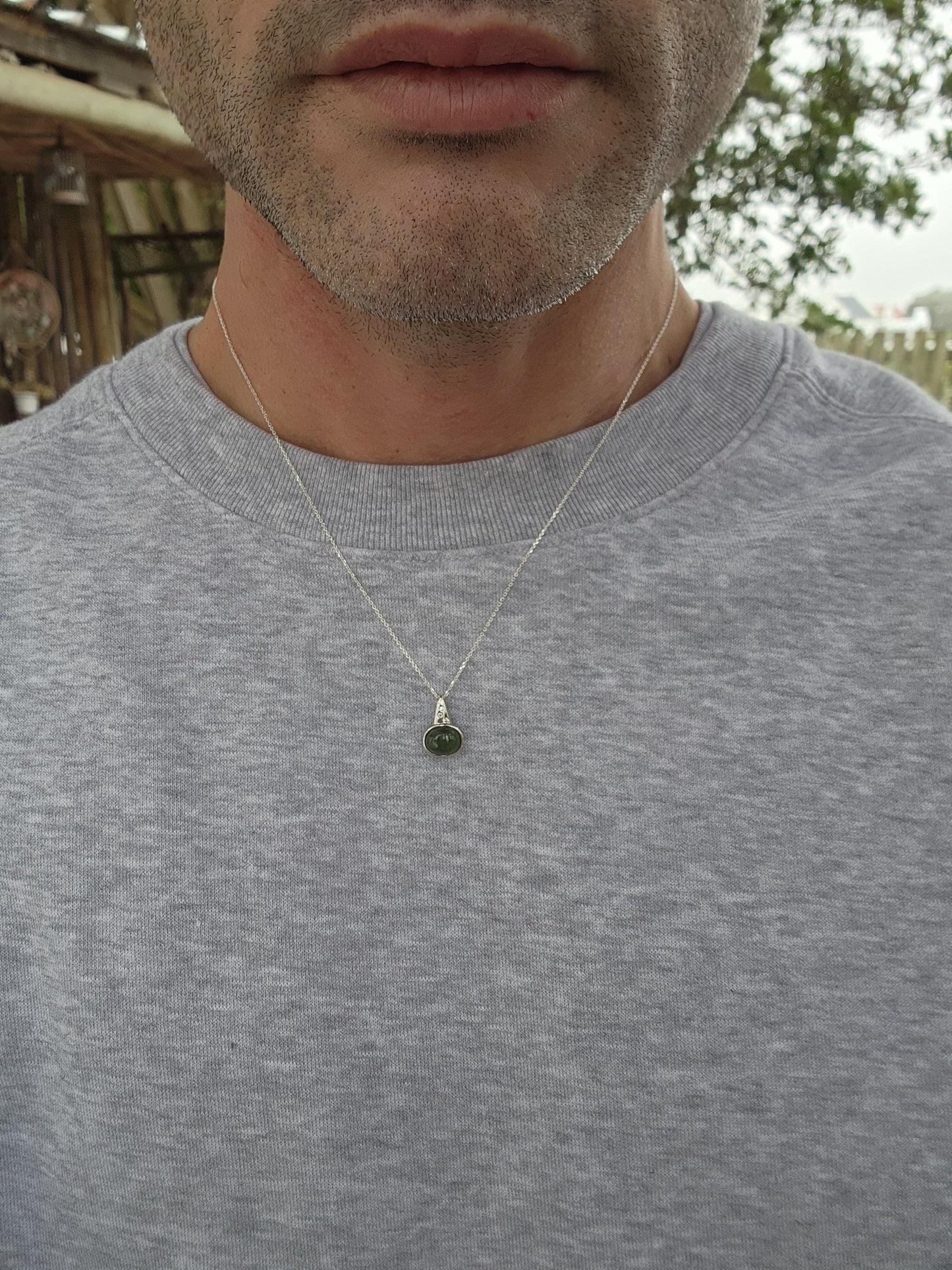 Sterling Silver pendant bezel/tube set with a Oval Shaped Green Nephrite Jade Cabochon , suspended from a Modernist Triangular shape that has been flush set with 3x CZ Gemstones.Comes fitted on a adjustable length Sterling Silver chain.