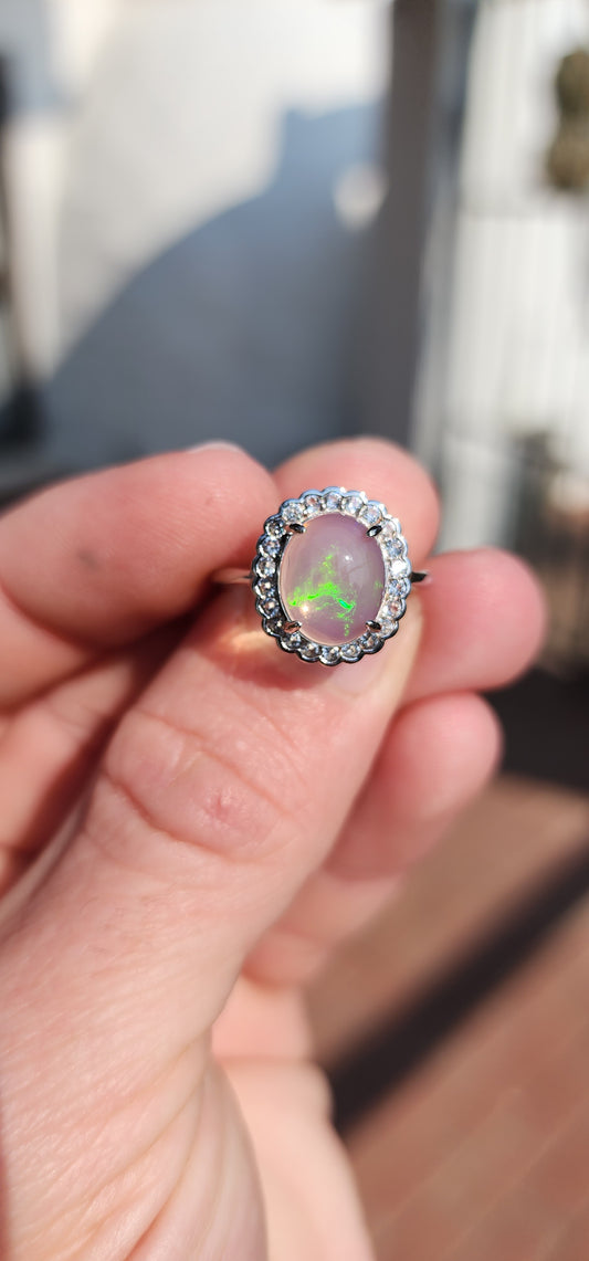 Impressive Ethiopian Water/Jelly Opal Cabochon and clear Round cut CZ haló Solitaire style ring .Crafted in Sterling Silver, the Oval Opal Cabochon is elegantly prong set and surrounded by an haló of 22x small Round cut CZ Gemstones.