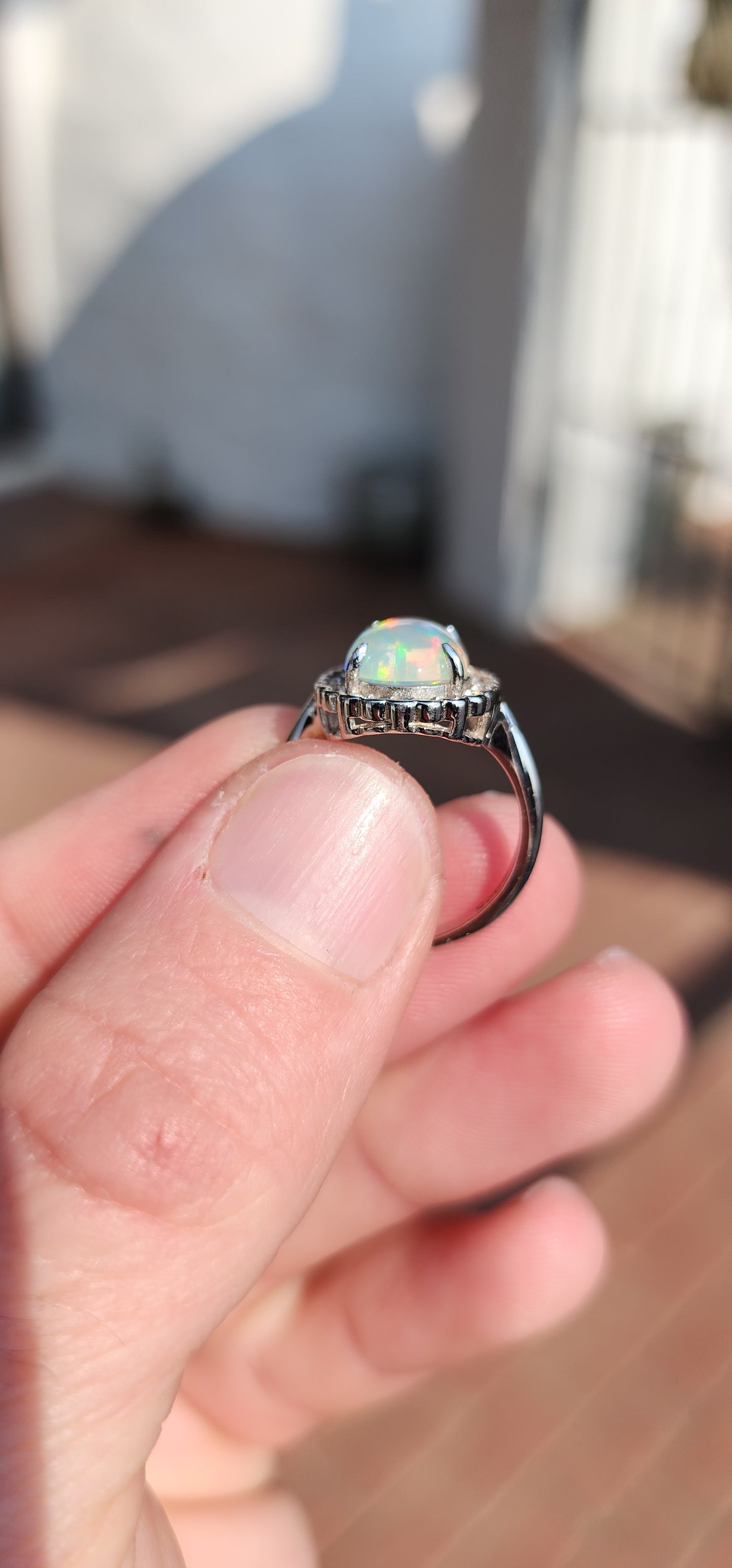 Impressive Ethiopian Water/Jelly Opal Cabochon and clear Round cut CZ haló Solitaire style ring .Crafted in Sterling Silver, the Oval Opal Cabochon is elegantly prong set and surrounded by an haló of 22x small Round cut CZ Gemstones.