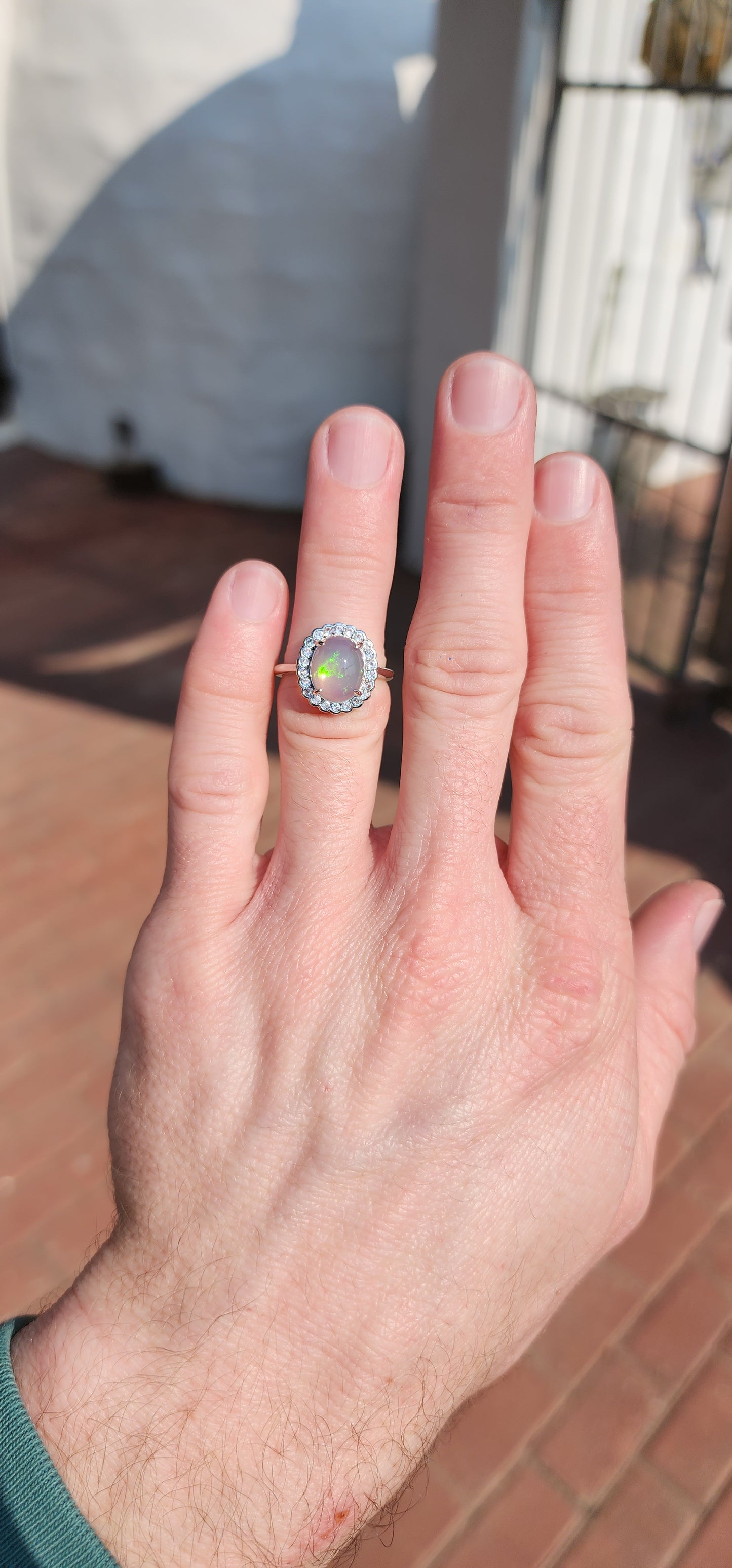 Impressive Ethiopian Water/Jelly Opal Cabochon and clear Round cut CZ haló Solitaire style ring .Crafted in Sterling Silver, the Oval Opal Cabochon is elegantly prong set and surrounded by an haló of 22x small Round cut CZ Gemstones.