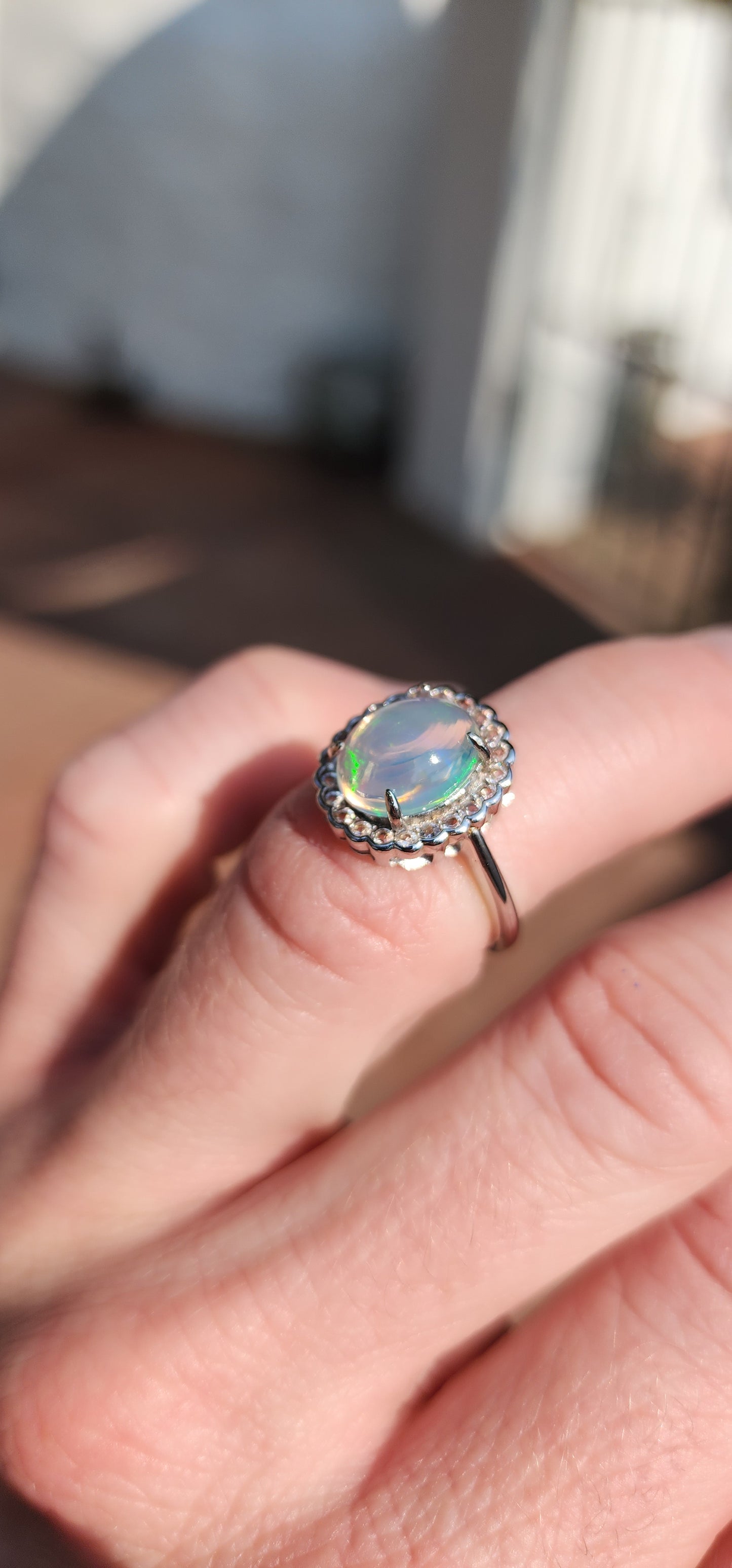 Impressive Ethiopian Water/Jelly Opal Cabochon and clear Round cut CZ haló Solitaire style ring .Crafted in Sterling Silver, the Oval Opal Cabochon is elegantly prong set and surrounded by an haló of 22x small Round cut CZ Gemstones.