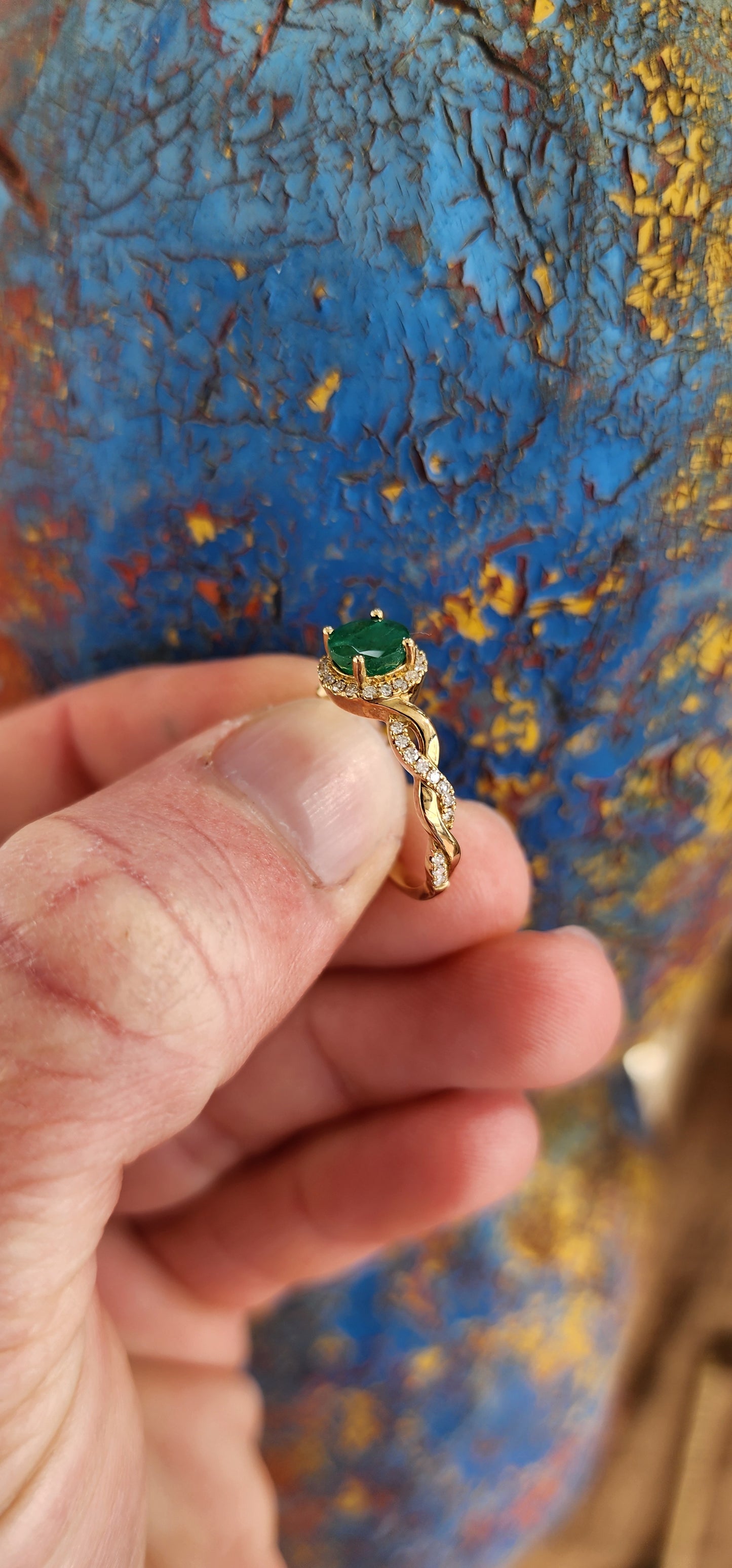 Exquisite 9ct Yellow Gold Crossover/Braided halo Ring, which boasts a mesmerizing prong set Round cut Emerald as its focal point,framed in a halo of small Brilliant Round cut Diamonds.