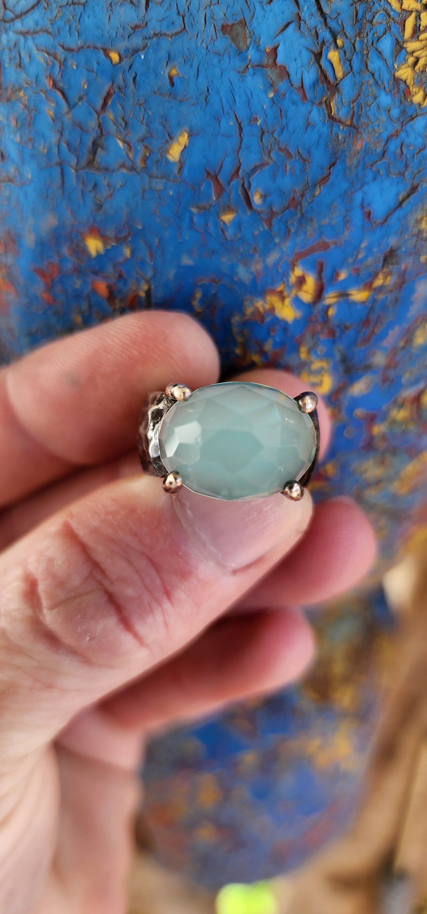 Glorious studio/artisan made statement ring.Crafted in Sterling Silver, the Black patinated band featuring a hammered/textured pattern , prong set in the centre is lovely Oval faceted cut Aqua Chalcedony Gemstone.