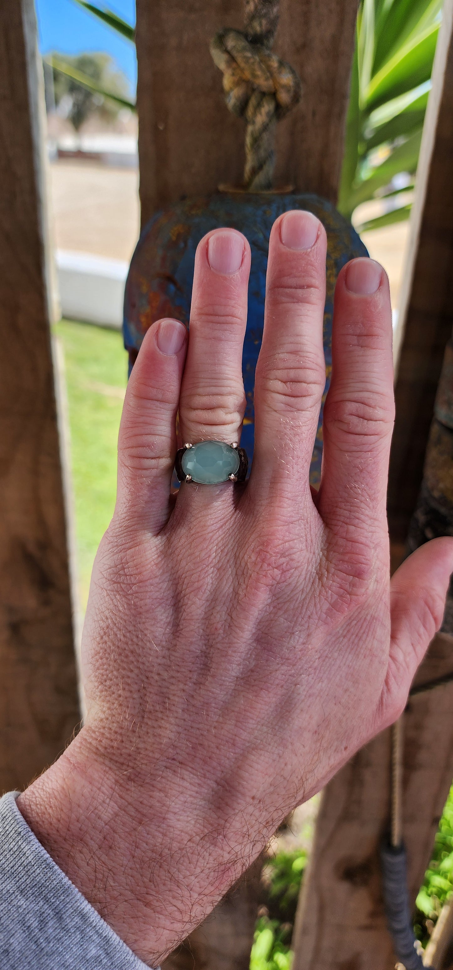 Glorious studio/artisan made statement ring.Crafted in Sterling Silver, the Black patinated band featuring a hammered/textured pattern , prong set in the centre is lovely Oval faceted cut Aqua Chalcedony Gemstone.