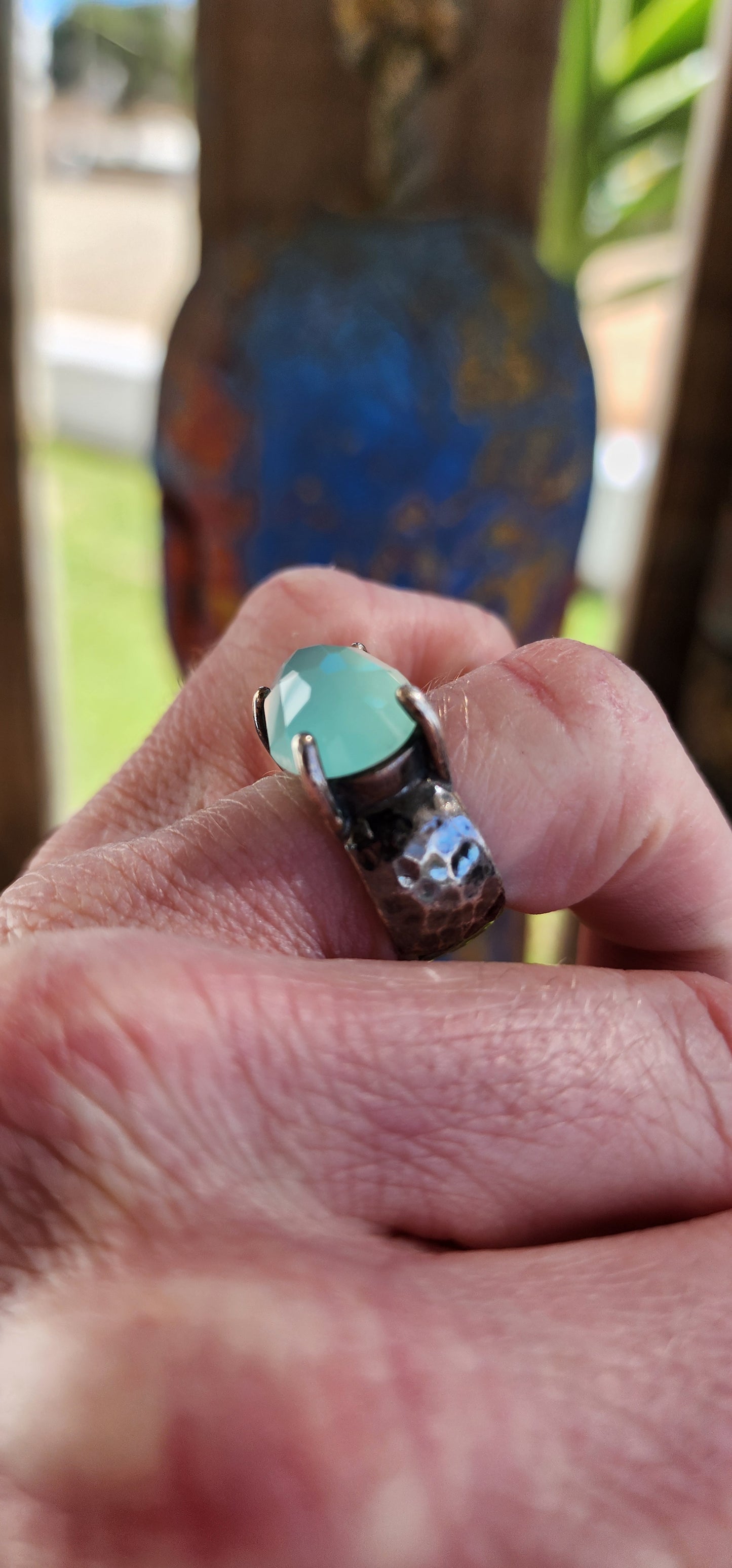 Glorious studio/artisan made statement ring.Crafted in Sterling Silver, the Black patinated band featuring a hammered/textured pattern , prong set in the centre is lovely Oval faceted cut Aqua Chalcedony Gemstone.