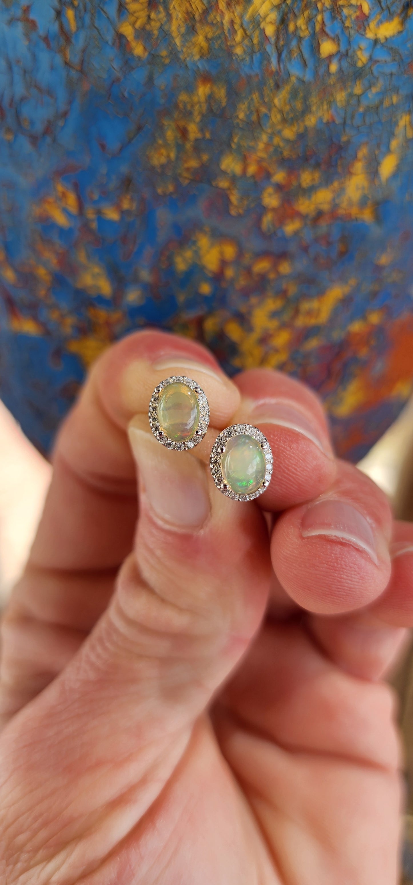 A glowing pair of Sterling Silver Halo earstuds composed of Ethiopian Opal Cabochons and sparkly CZ Gemstones in a Oval layout. Each piece features a Ethiopian Opal Cabochon prong set in the centre, surrounded by a Halo of Round CZ Gemstones.