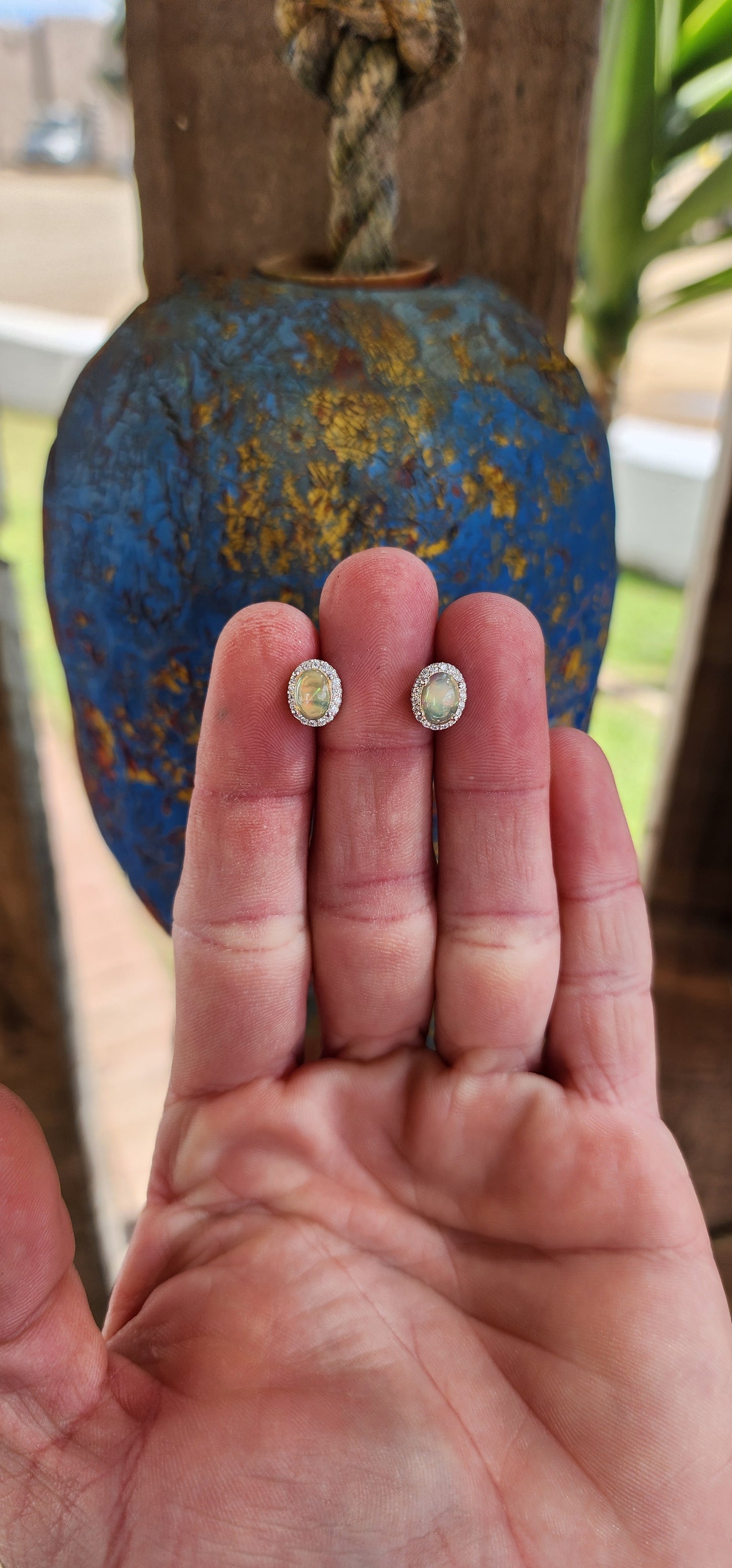 A glowing pair of Sterling Silver Halo earstuds composed of Ethiopian Opal Cabochons and sparkly CZ Gemstones in a Oval layout. Each piece features a Ethiopian Opal Cabochon prong set in the centre, surrounded by a Halo of Round CZ Gemstones.