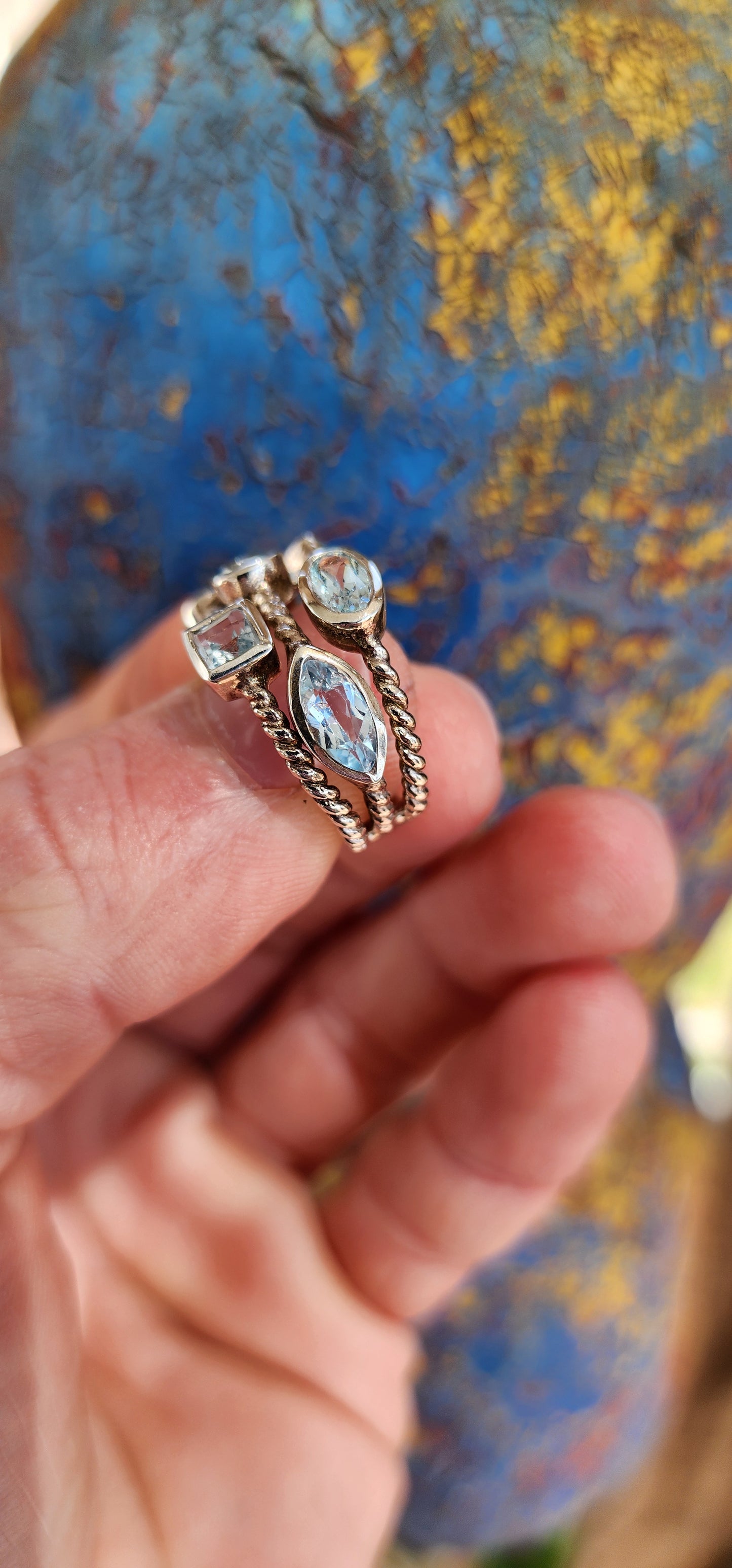 This unique Sterling Silver cluster ring features a Rope pattern on three bands and is adorned with Sky Blue Topaz Gemstones in various shapes and sizes.
The Topaz Gemstones being bezel/tube set.