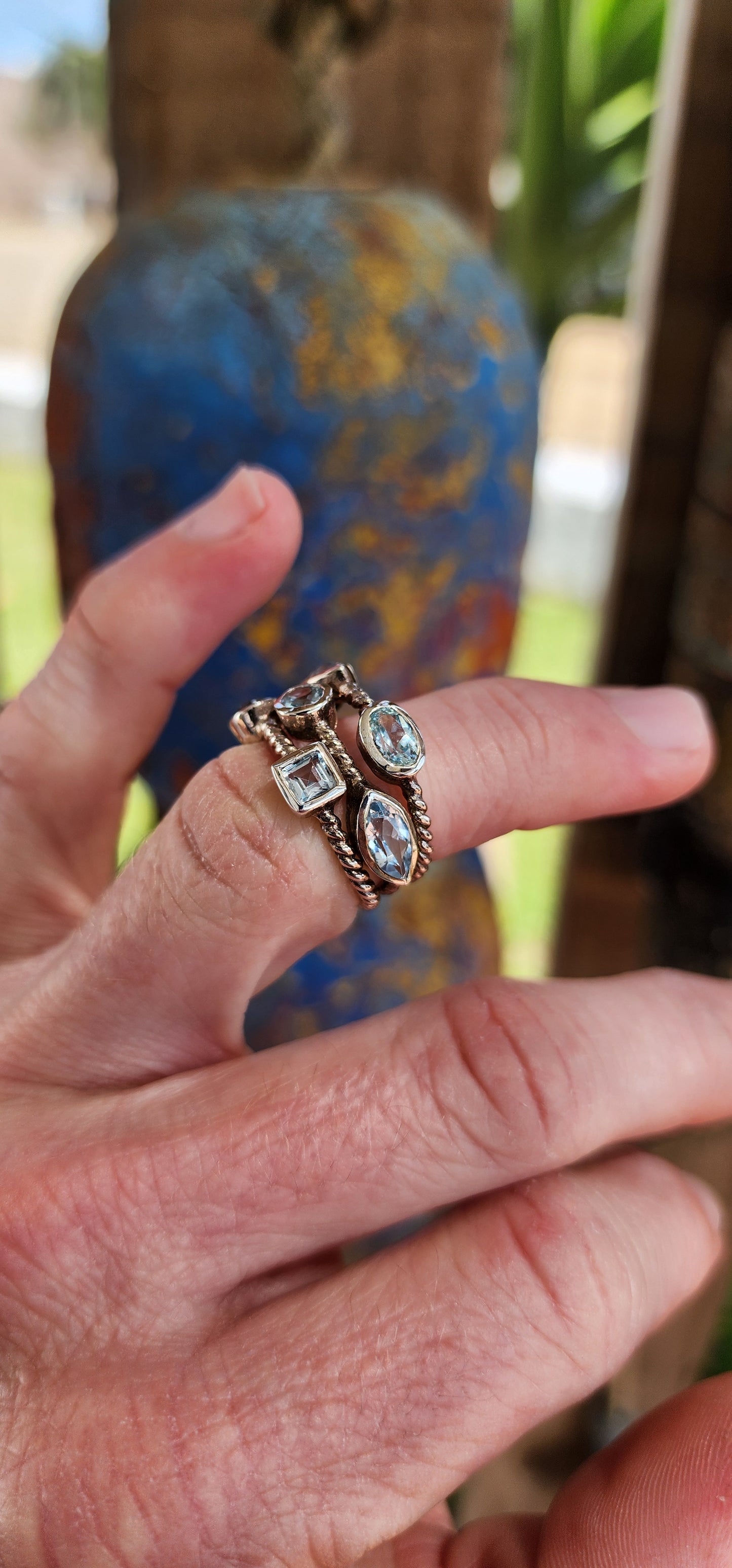 This unique Sterling Silver cluster ring features a Rope pattern on three bands and is adorned with Sky Blue Topaz Gemstones in various shapes and sizes.
The Topaz Gemstones being bezel/tube set.