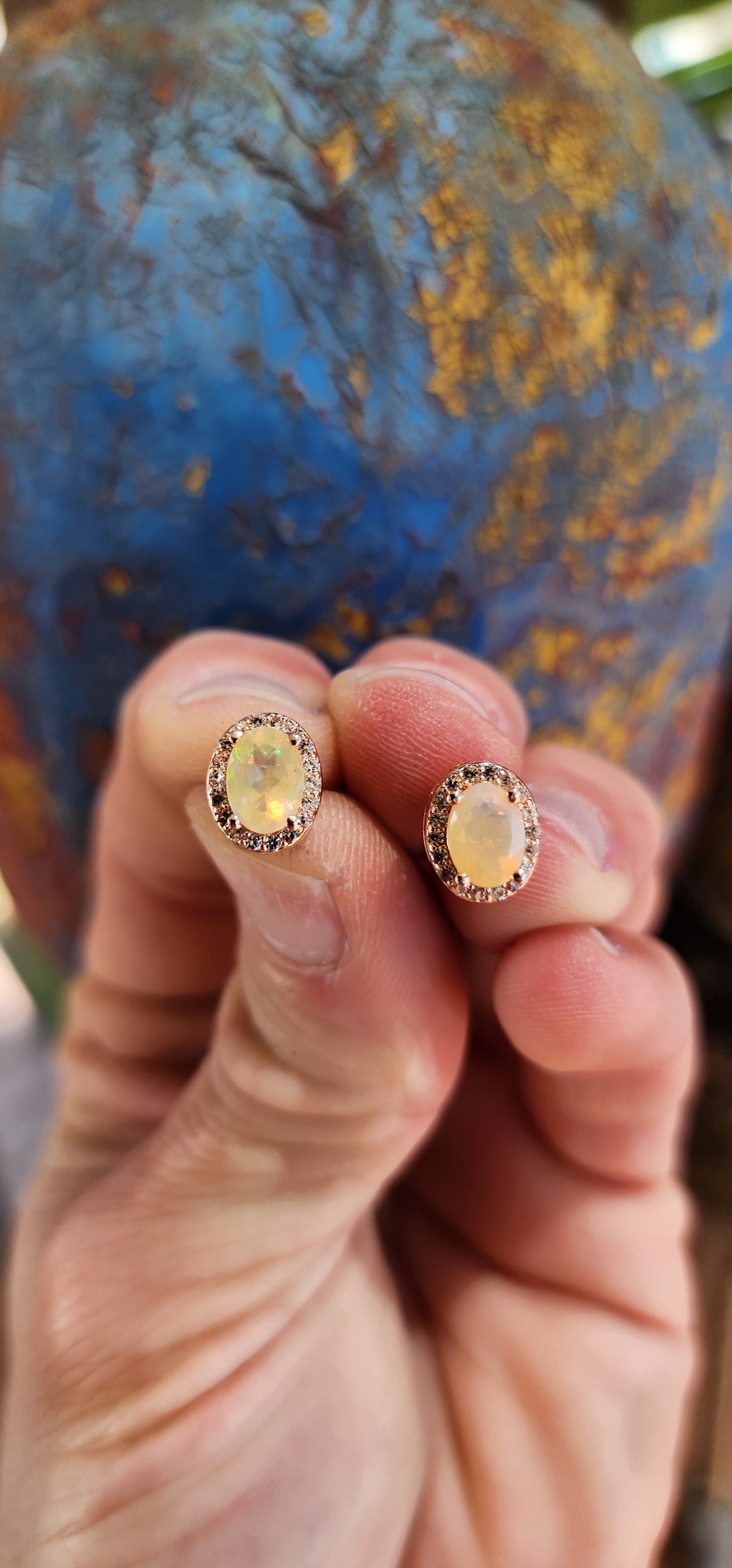 A glowing pair of Sterling Silver and Rose Gold plated Halo earstuds composed of Ethiopian faceted Opals and sparkly CZ Gemstones in a Oval layout. Each piece features a Ethiopian Opal prong set in the centre, surrounded by a halo of Round CZ Gemstones.