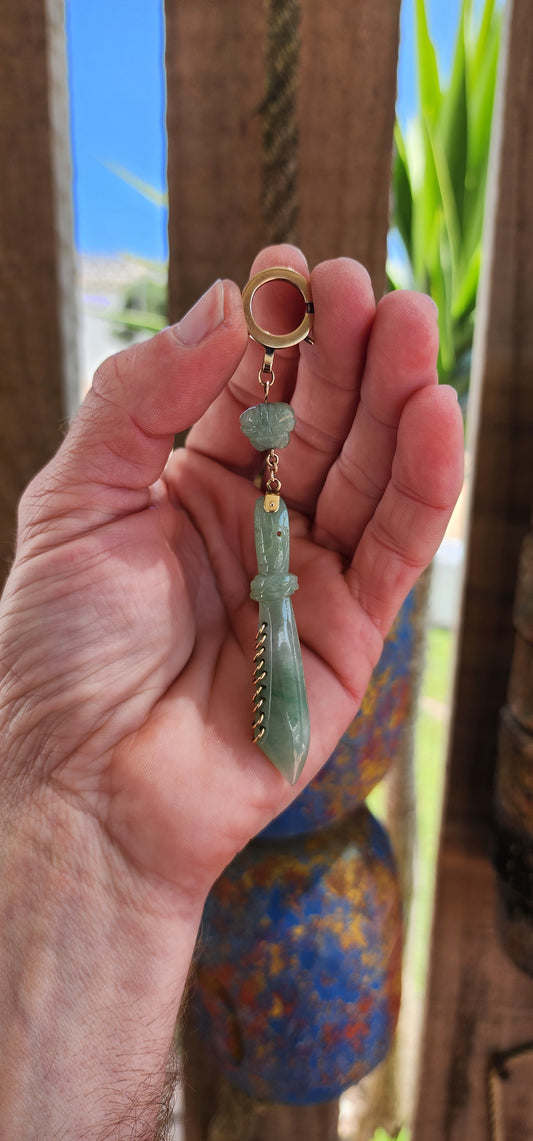 This pendant is a late Victorian-era piece featuring hand-carved jade and 9ct yellow gold. It’s crafted in the shape of a traditional Chinese nine-ring broadsword, with an apple-green jade blade.