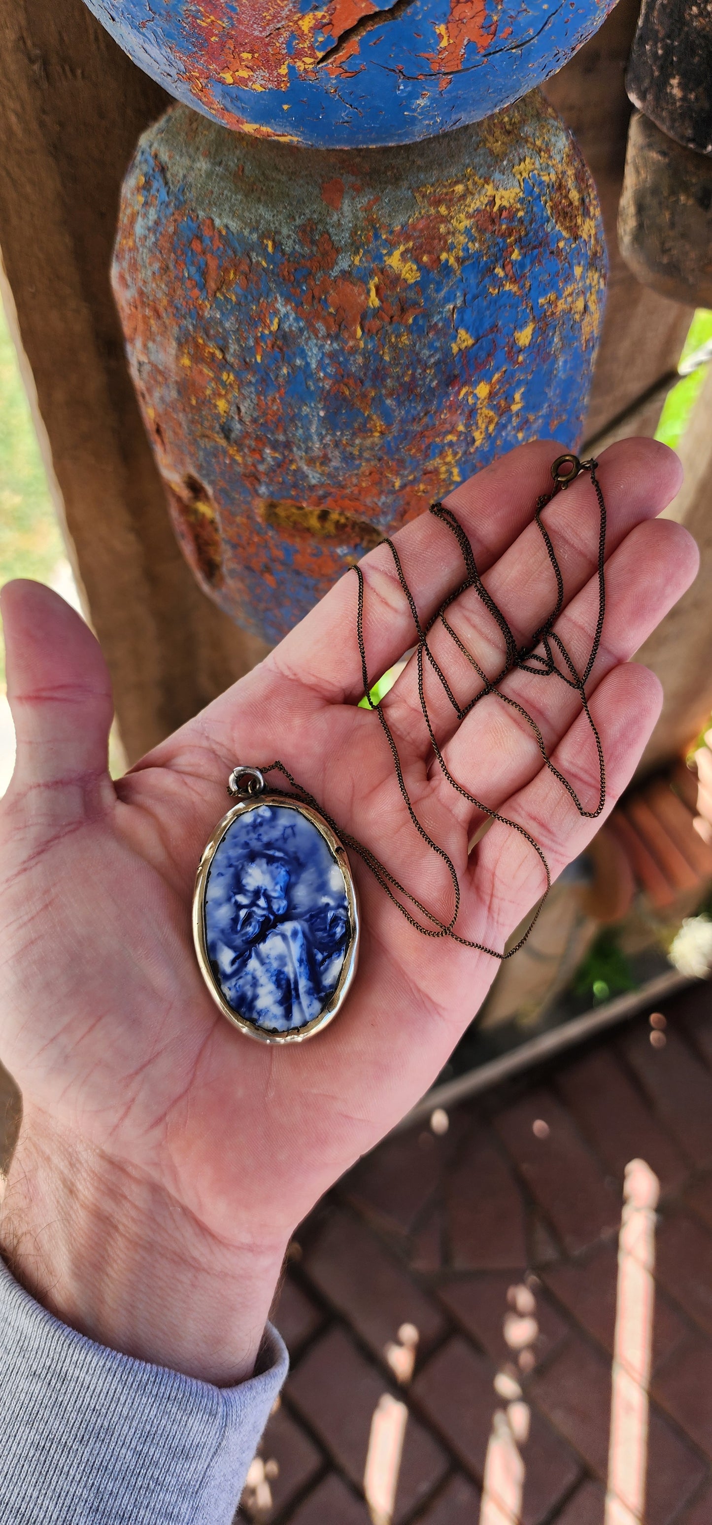 This unique Designer artisan-made pendant is a striking blend of artistry and cultural homage. Its oval shape frames a captivating blue glazed ceramic panel that presents an embossed depiction of an oriental figure.